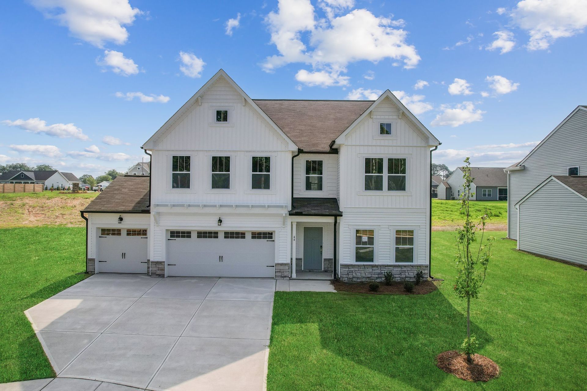 A large white house with a brown roof is sitting on top of a lush green field.