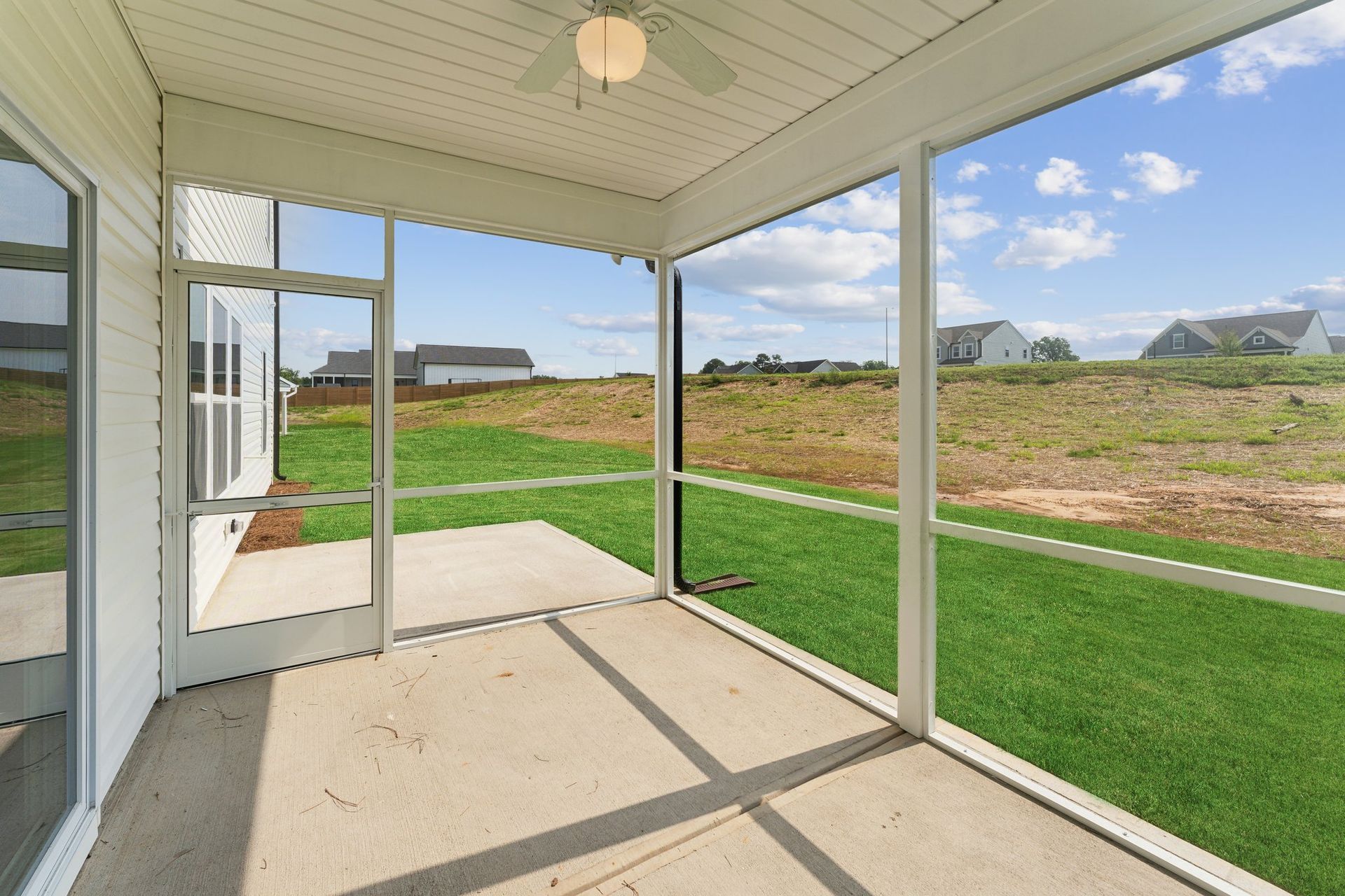 A screened in porch with a ceiling fan and a view of a grassy field.