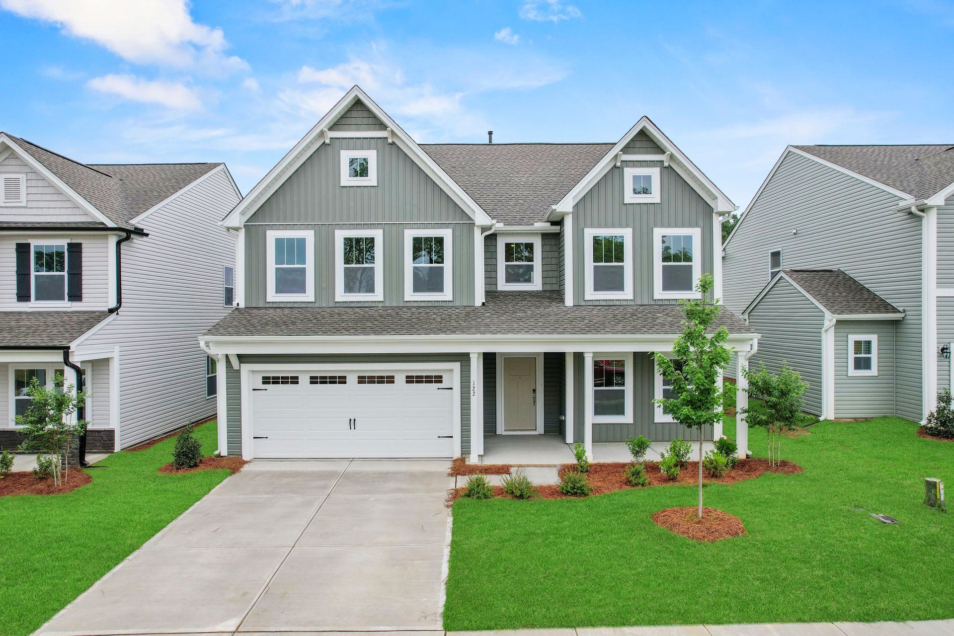 A large gray house with a white garage door is sitting on top of a lush green lawn.