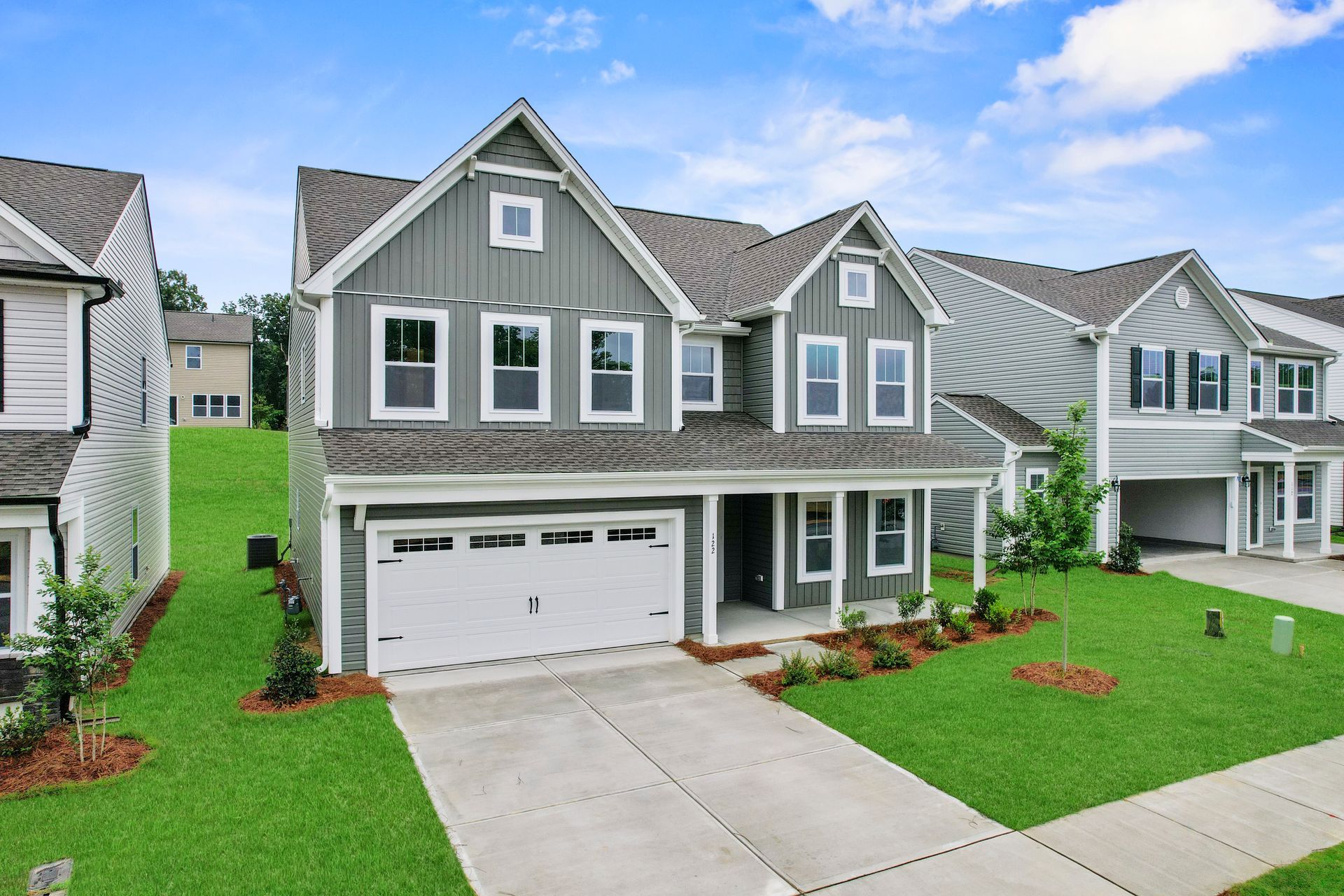 A large gray house with a white garage is sitting on top of a lush green field.