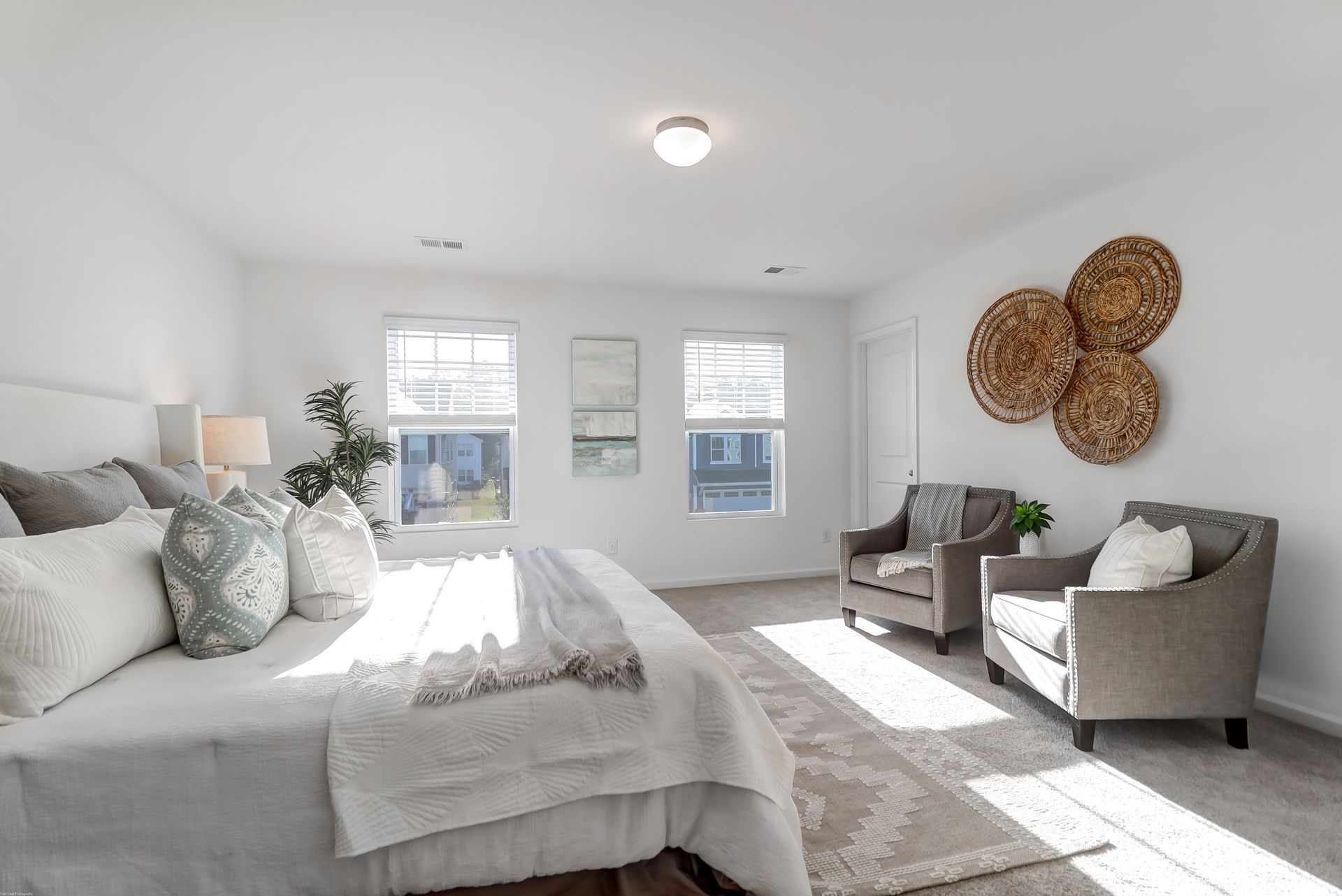 A bedroom with a large bed , two chairs , and two windows.