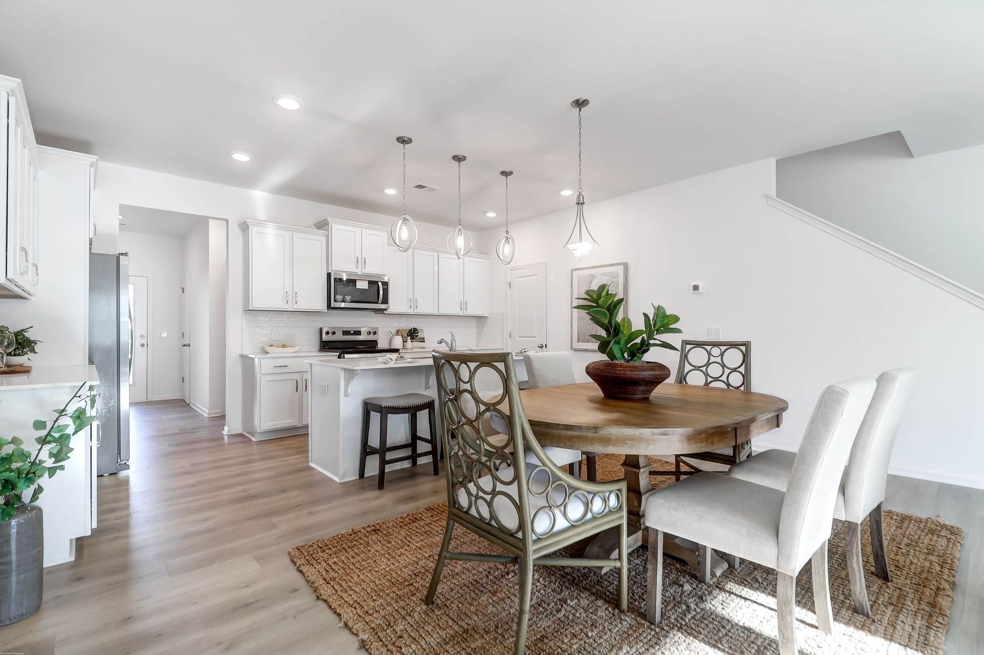 A dining room with a table and chairs and a kitchen in the background.