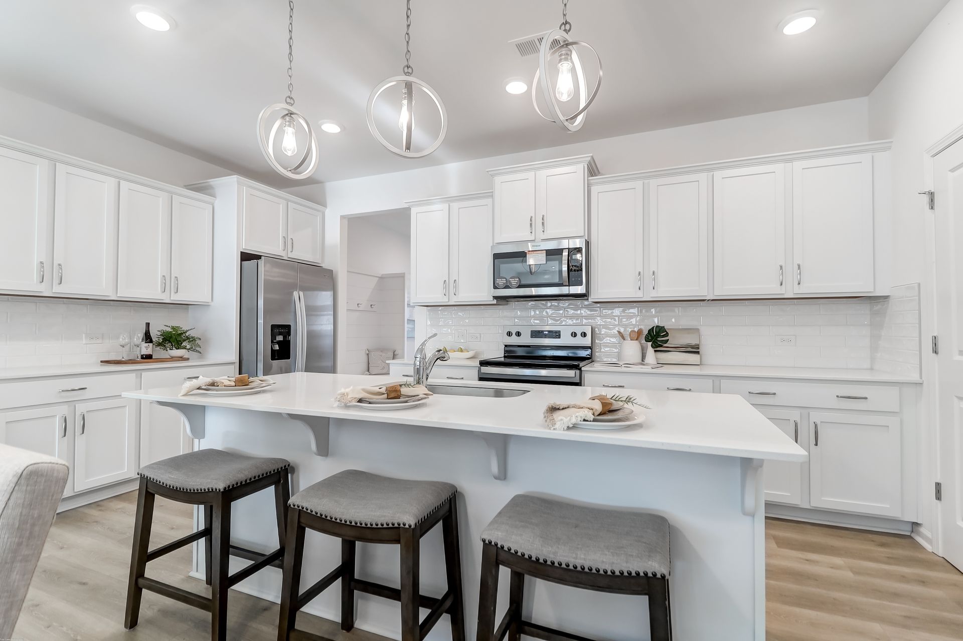 A kitchen with white cabinets and stools and a large island.
