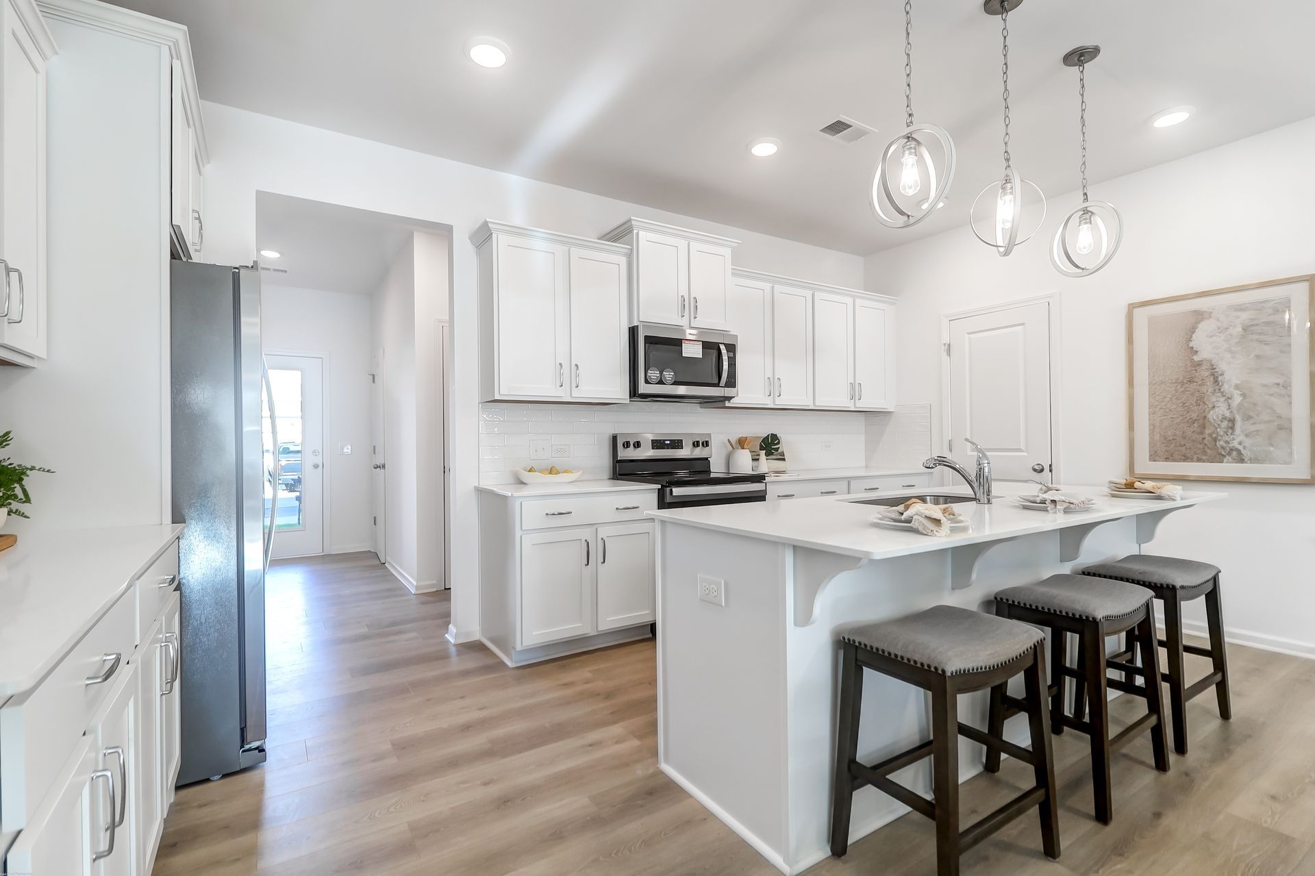 A kitchen with white cabinets , stools and a large island.
