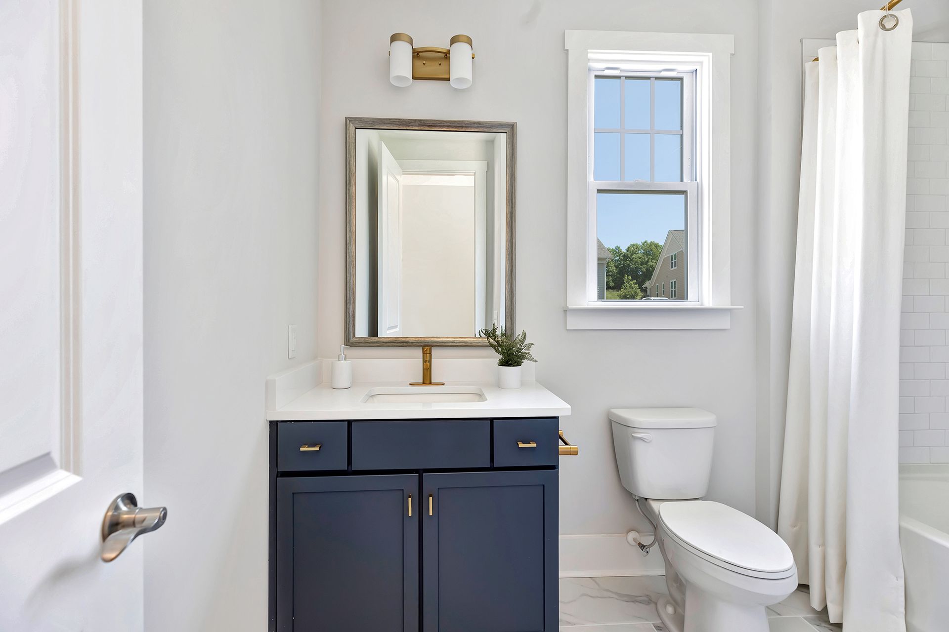 A bathroom with a sink , toilet , mirror and window.