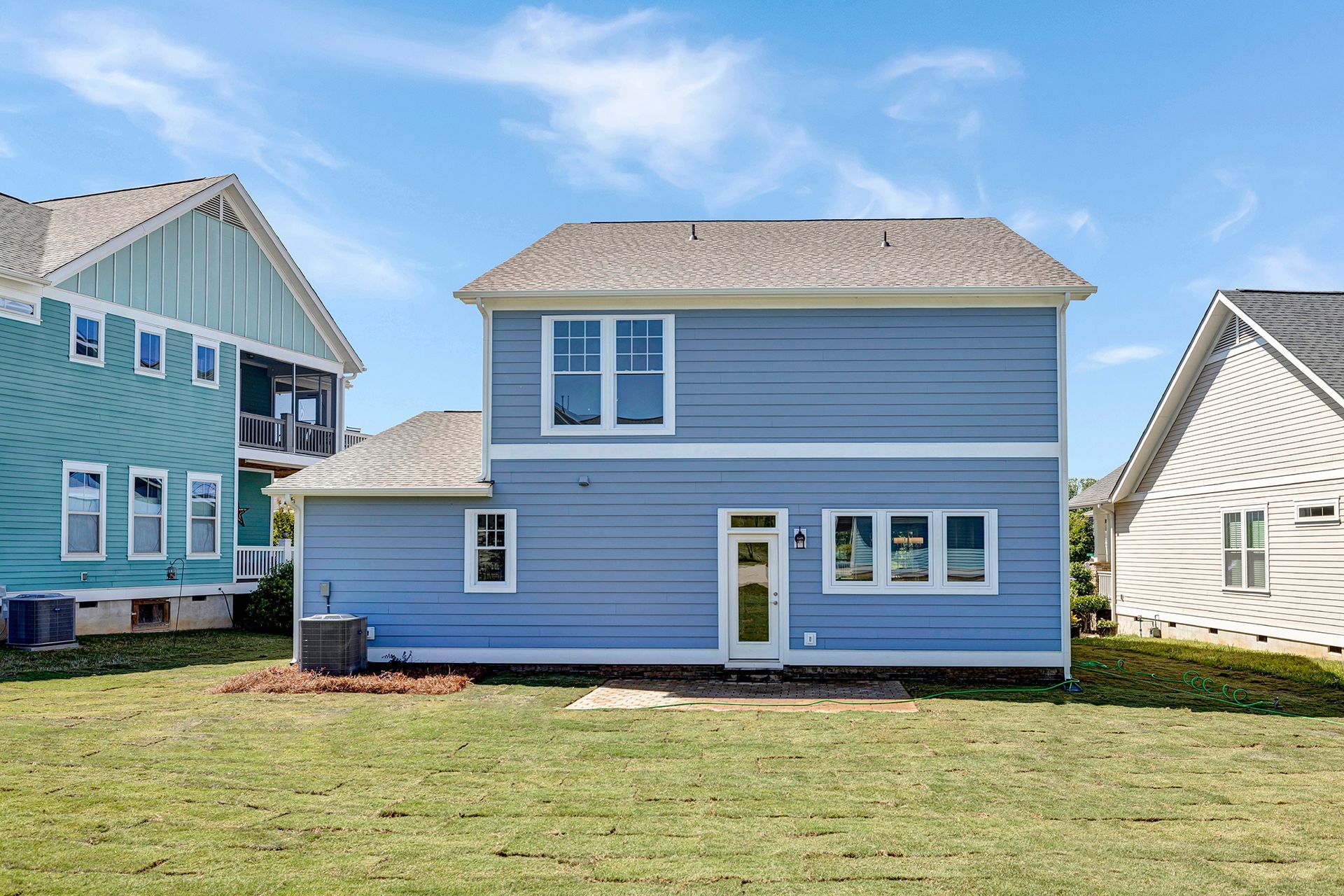 A blue and white house with a lot of windows is sitting on top of a lush green field.