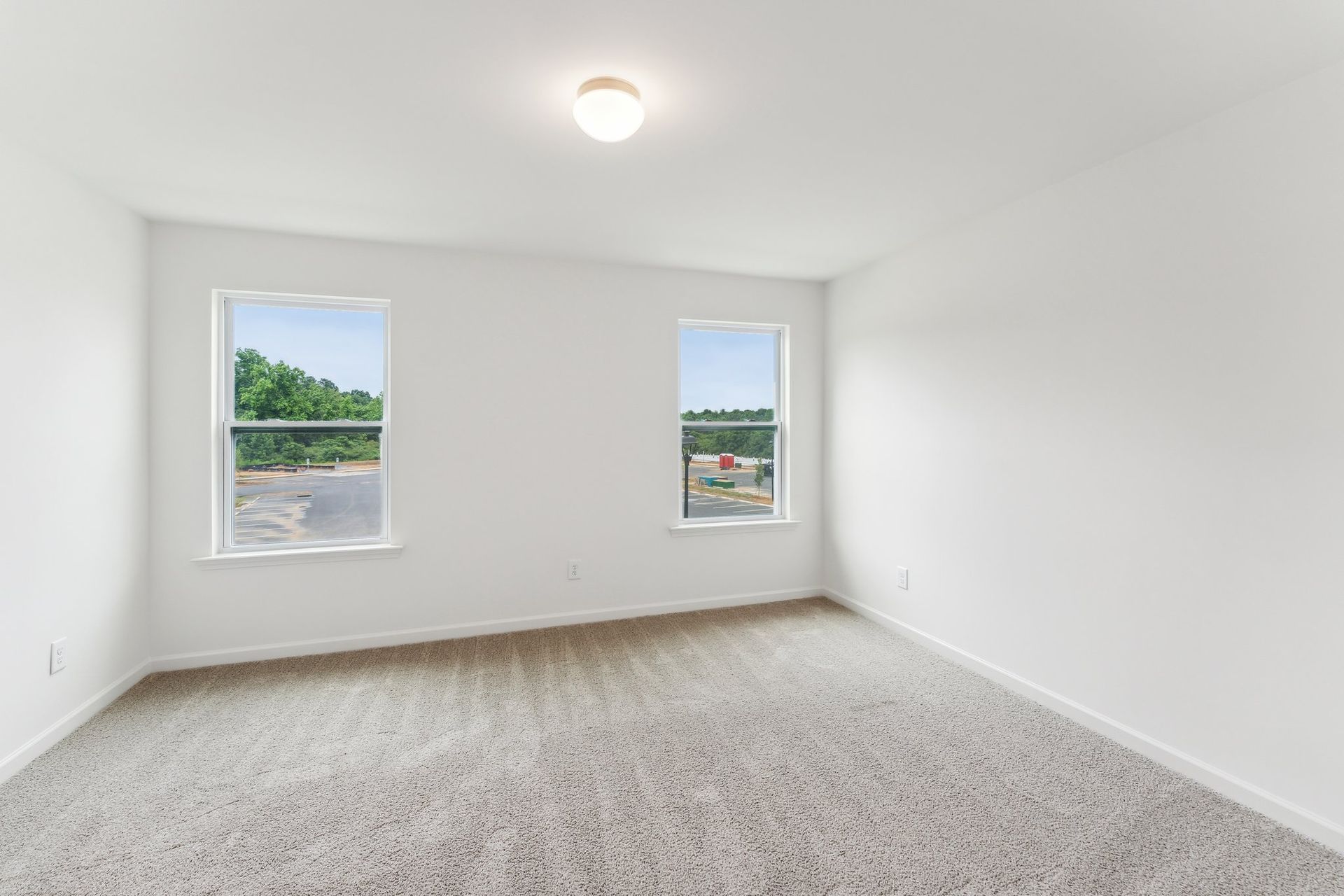 An empty bedroom with two windows and a carpeted floor.
