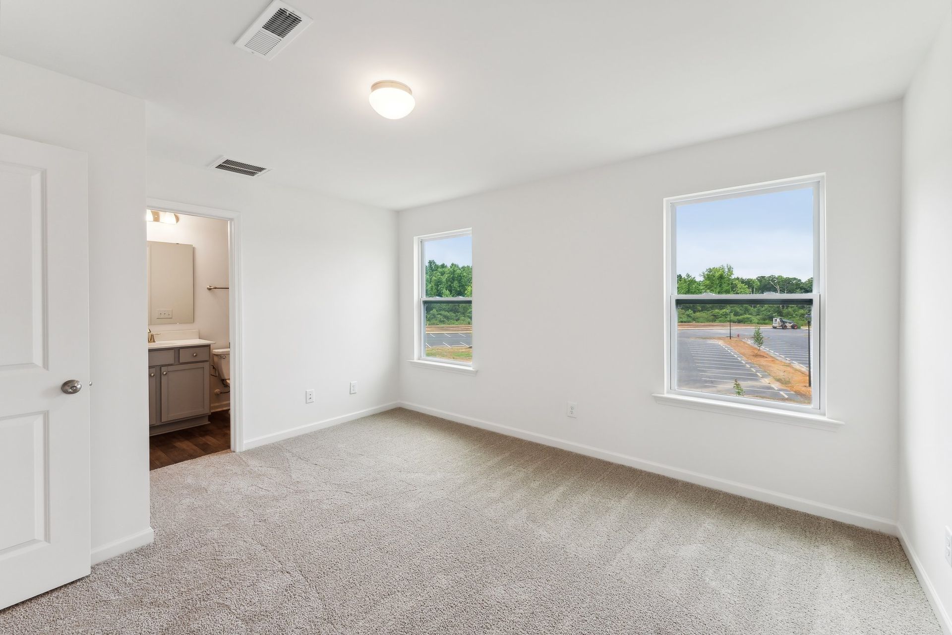 An empty bedroom with two windows and a carpeted floor.