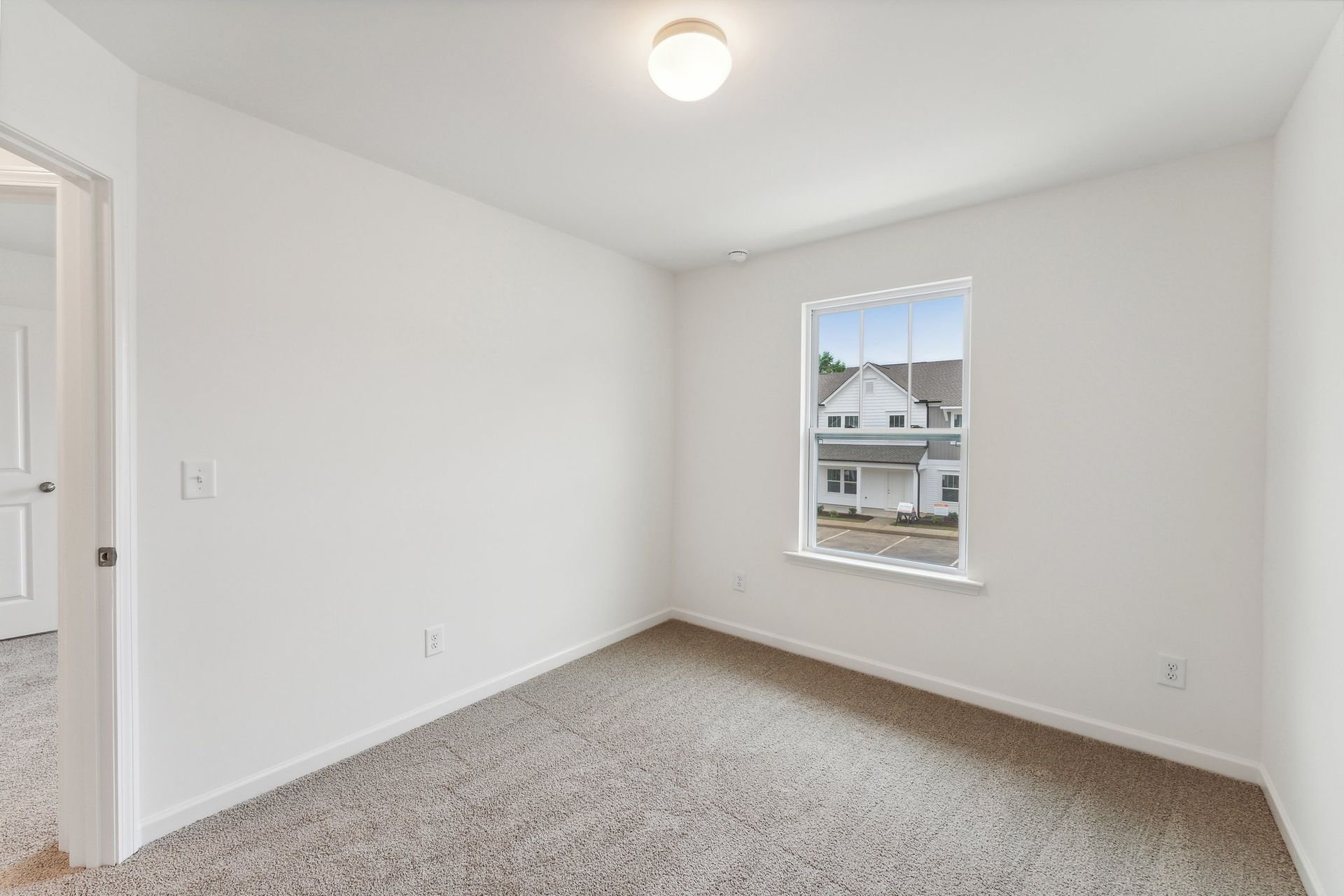 An empty bedroom with a window and a carpeted floor.