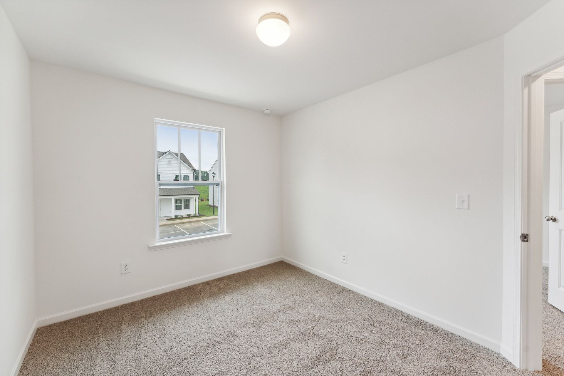 An empty bedroom with a window and a carpeted floor.