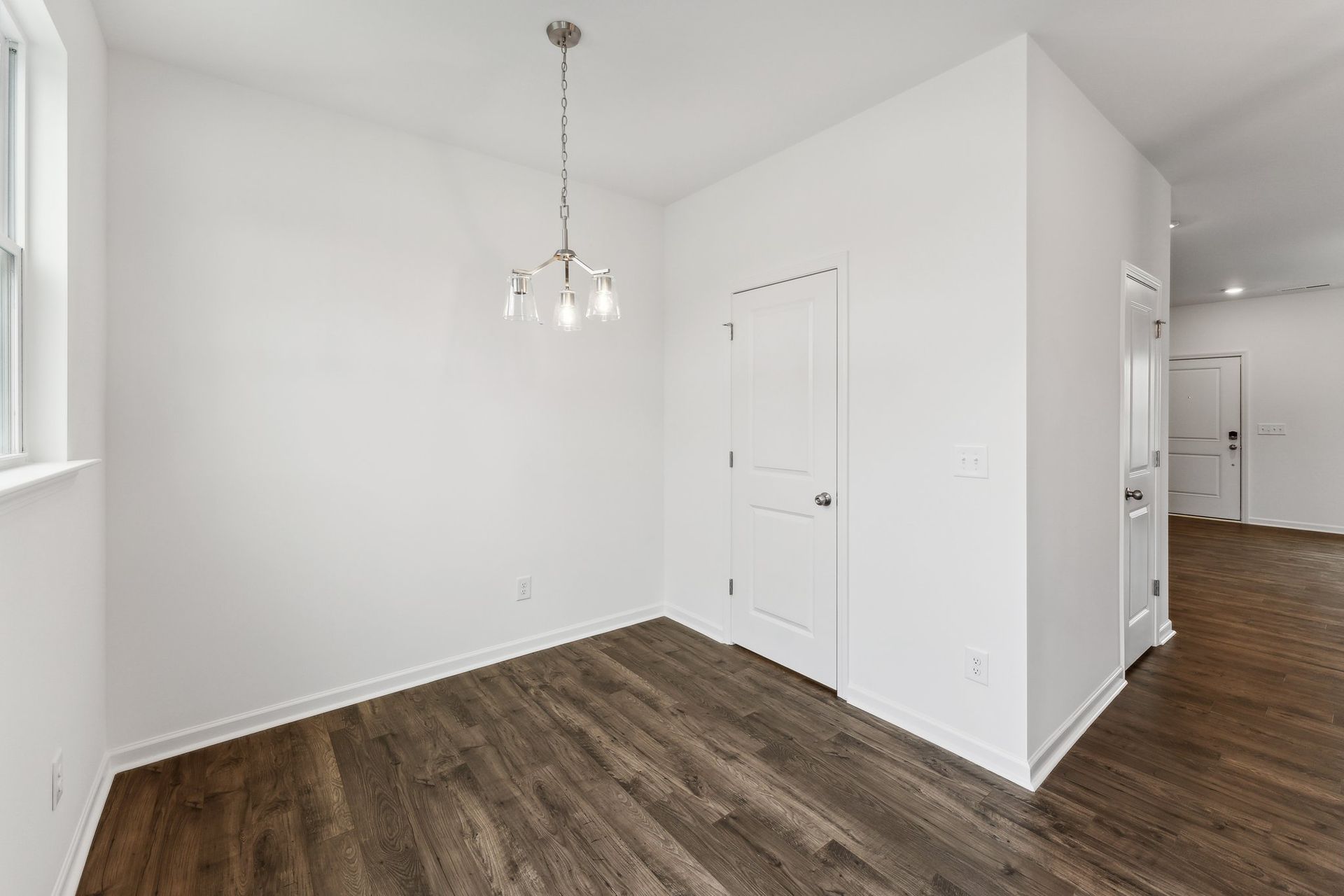 An empty dining room with hardwood floors and white walls.