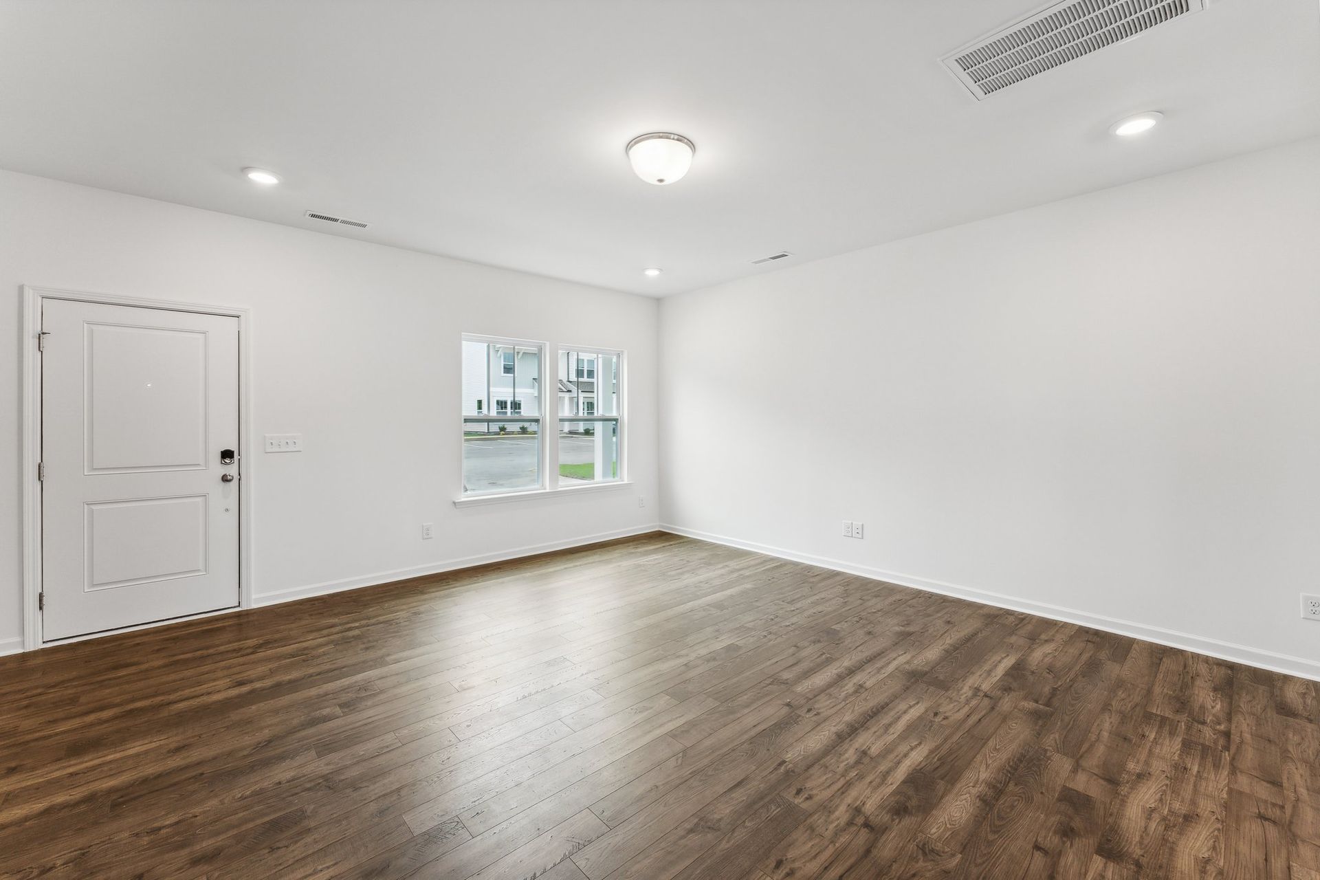 An empty living room with hardwood floors and white walls.