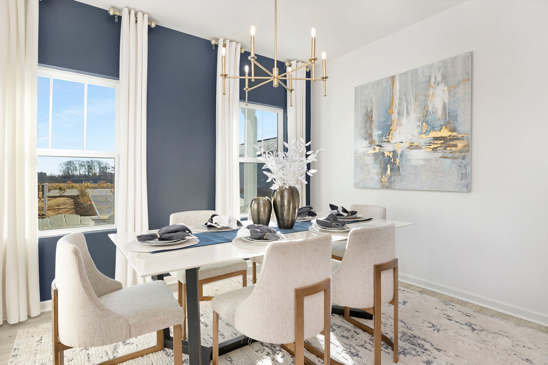 A dining room with a table and chairs and a painting on the wall.