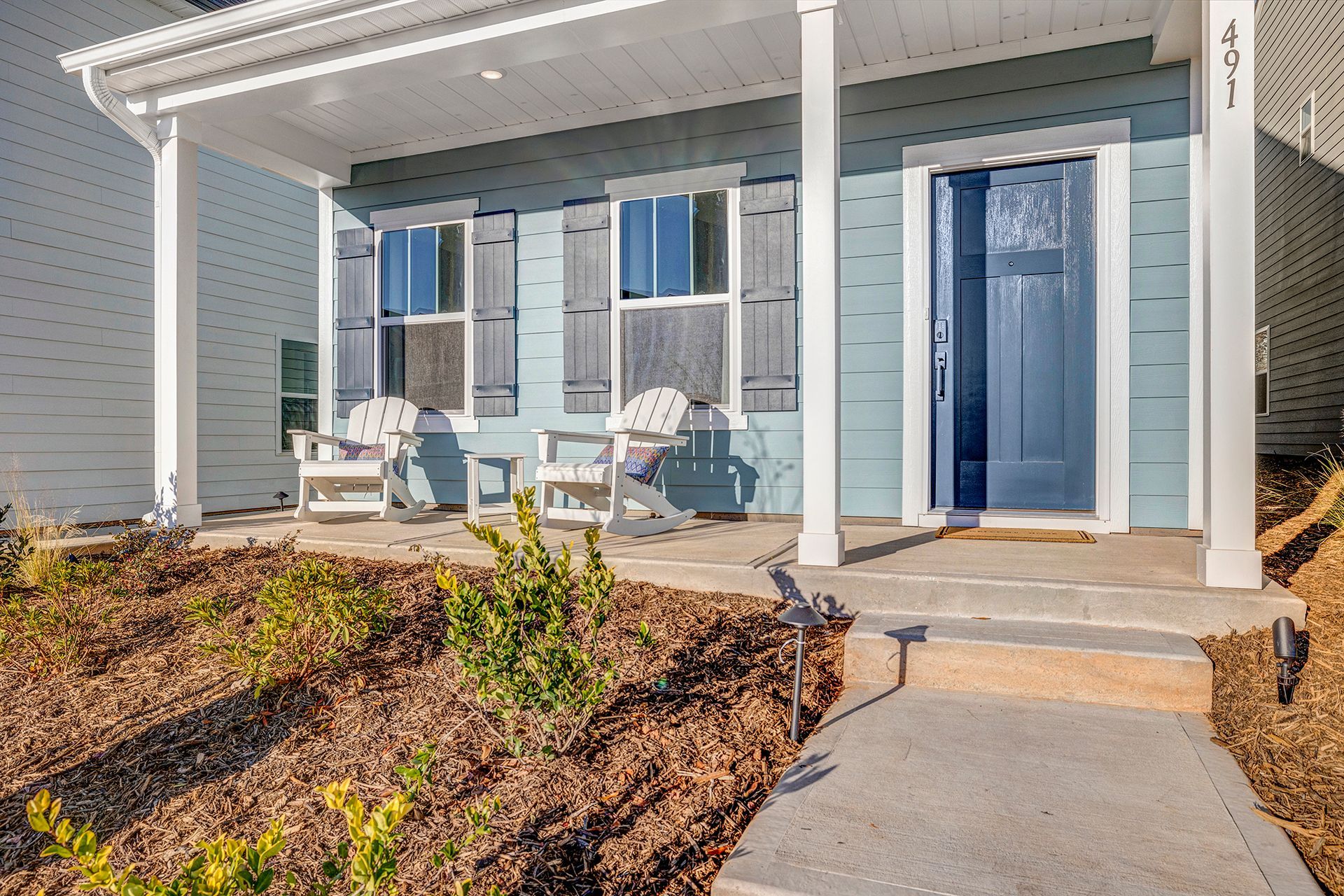 A blue house with white shutters and a porch with chairs.