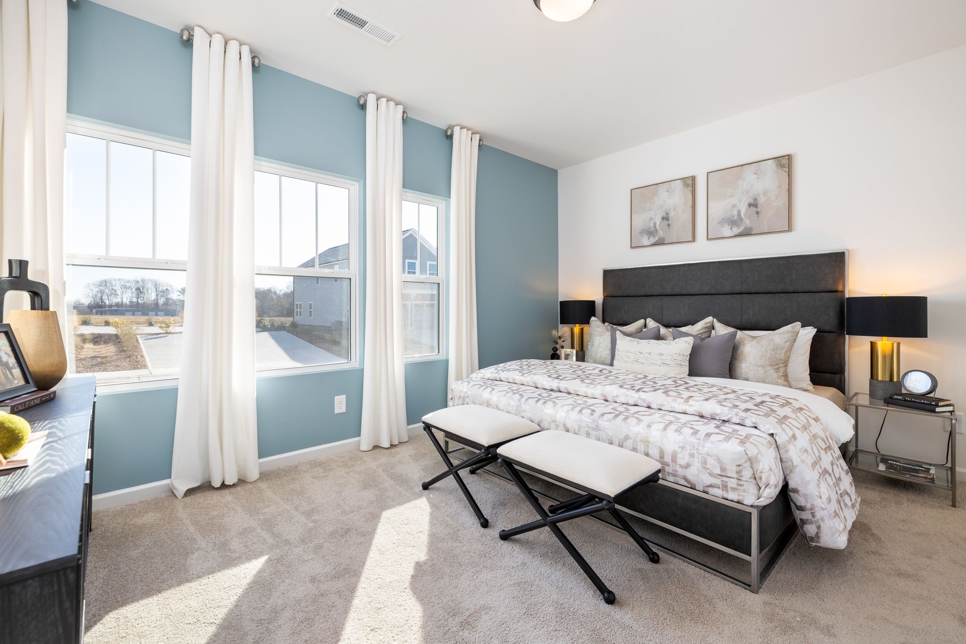 A bedroom with a king size bed , a dresser , two windows and a bench.
