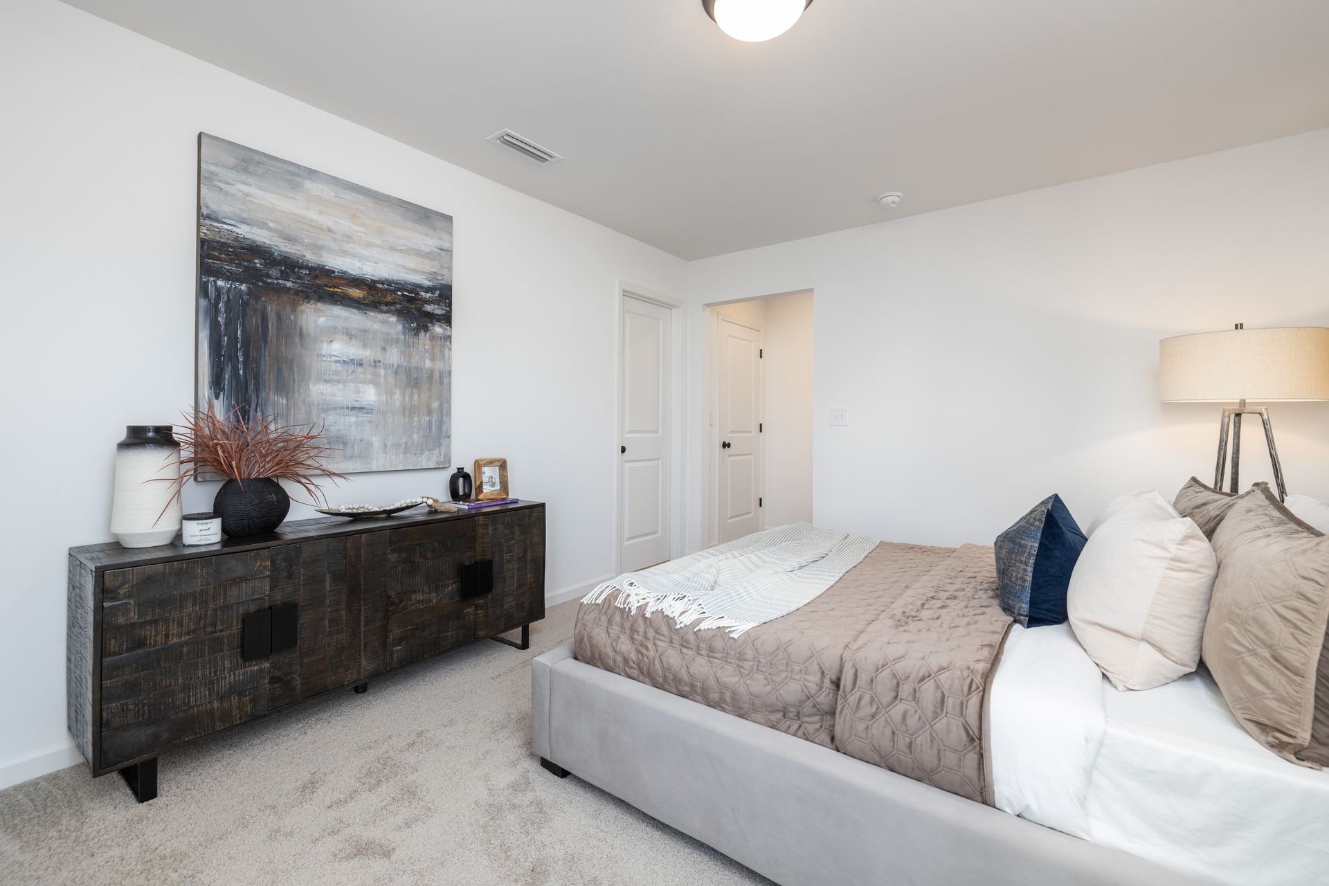 A bedroom with a bed , dresser , lamp and painting on the wall.