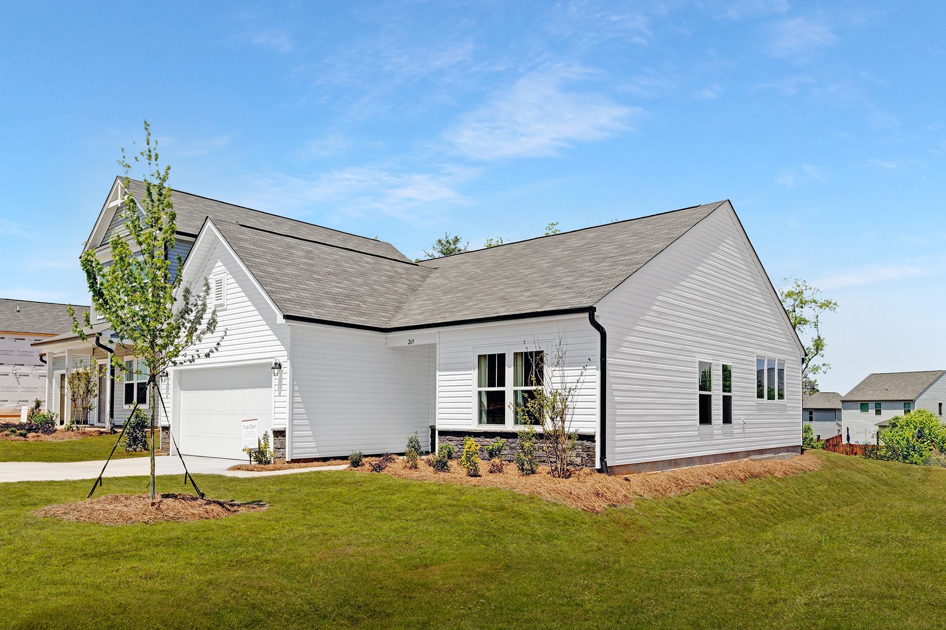 A white house with a gray roof is sitting on top of a lush green field.