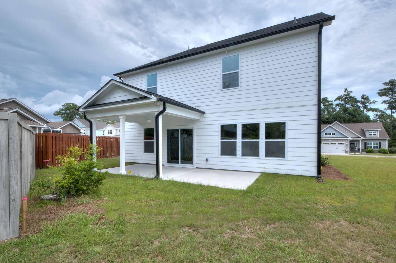 The back of a white house with a covered patio and a fence.