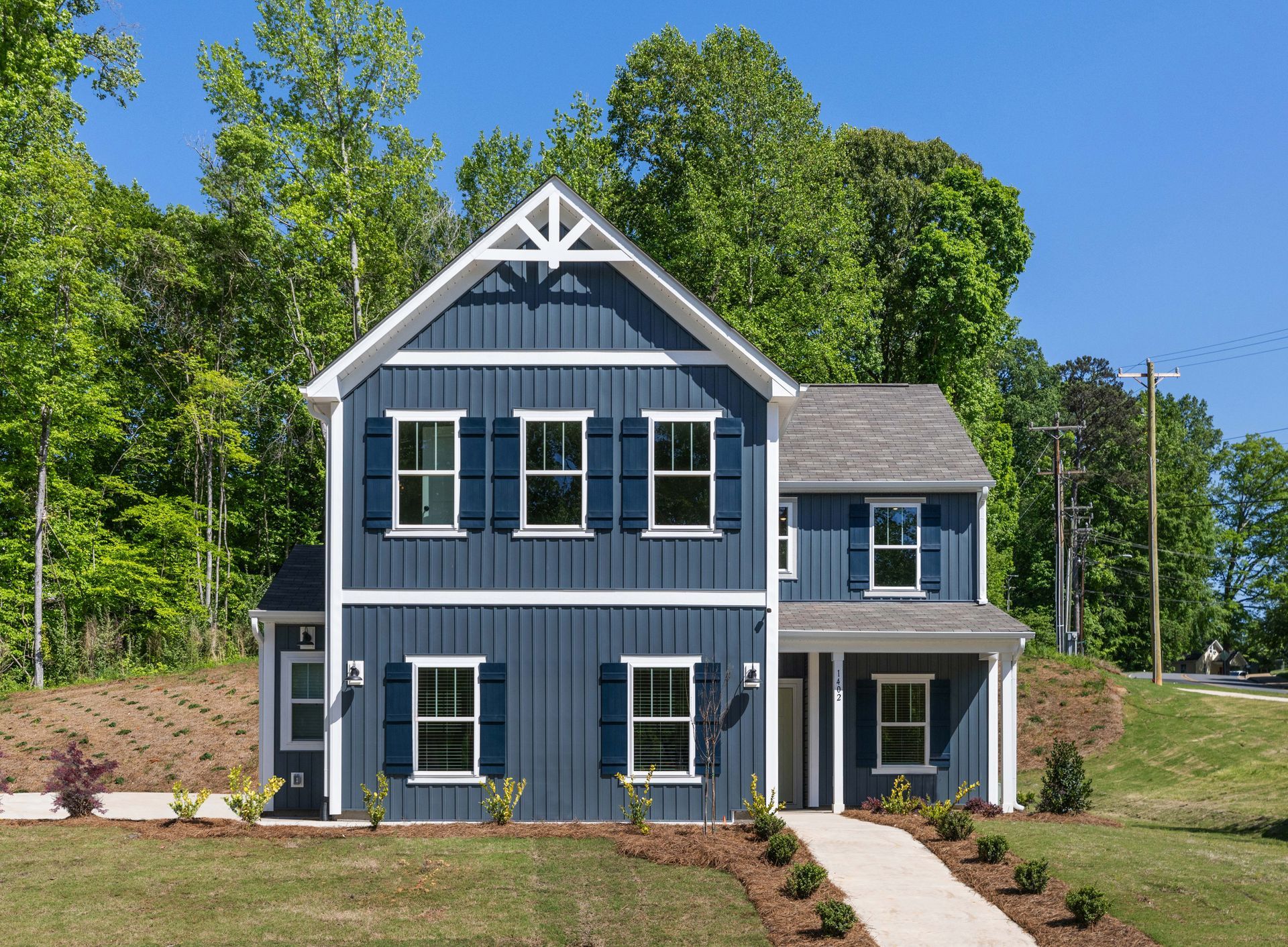 A blue and white house with a walkway leading to it is surrounded by trees.