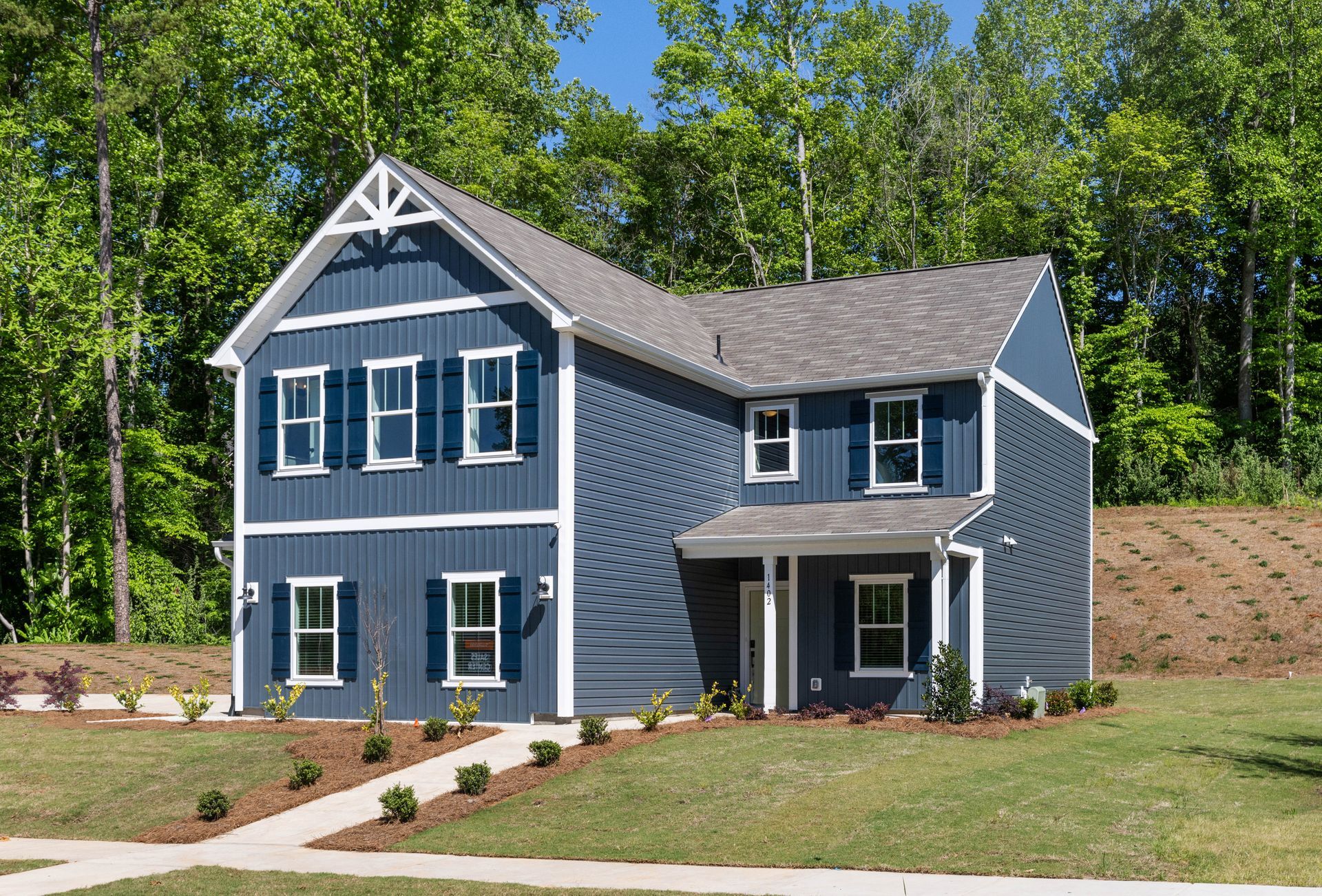 A blue house with white shutters is sitting on top of a lush green hillside.