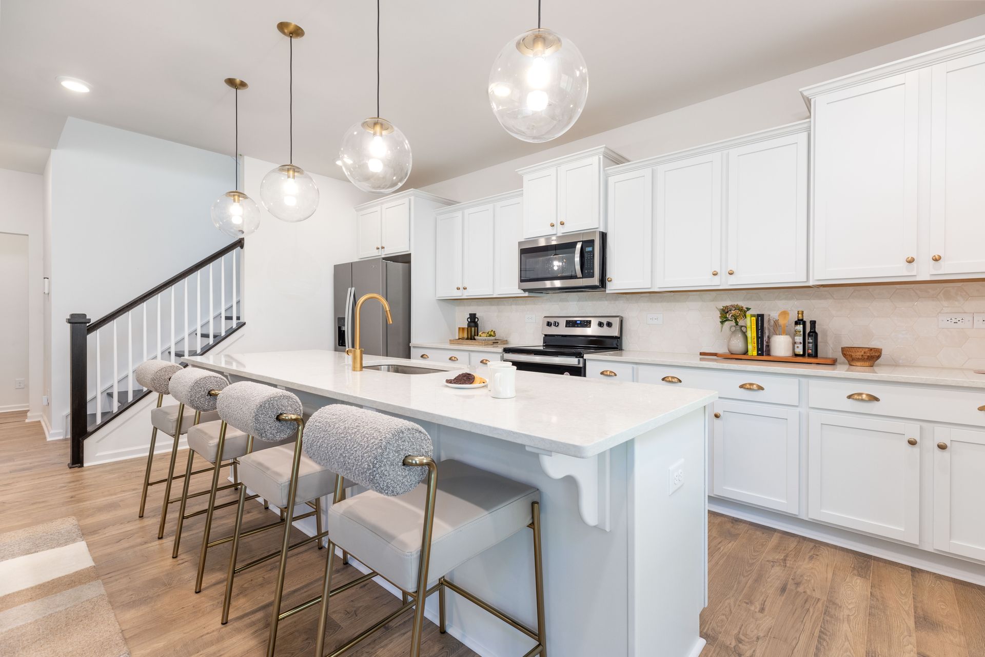 A kitchen with white cabinets , a large island , stools and a staircase.
