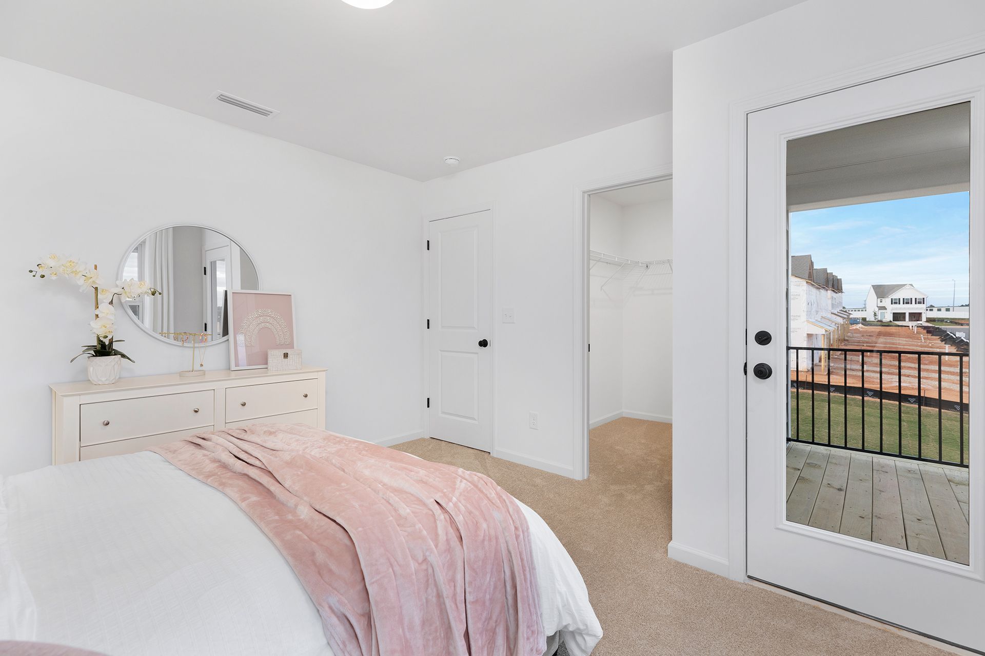 A bedroom with a bed , dresser , mirror and balcony.