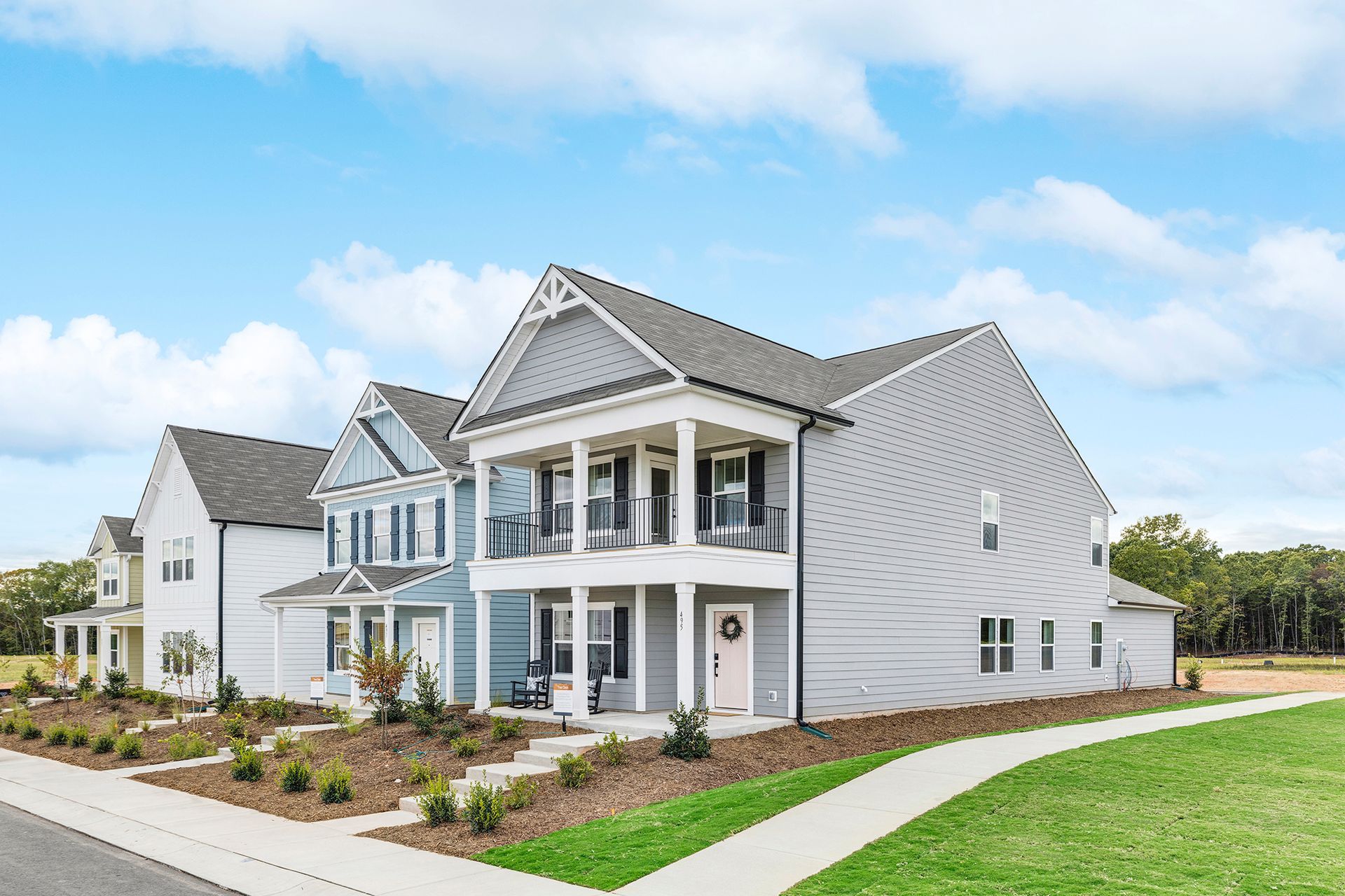 A large white house with a large porch is sitting on top of a lush green field.