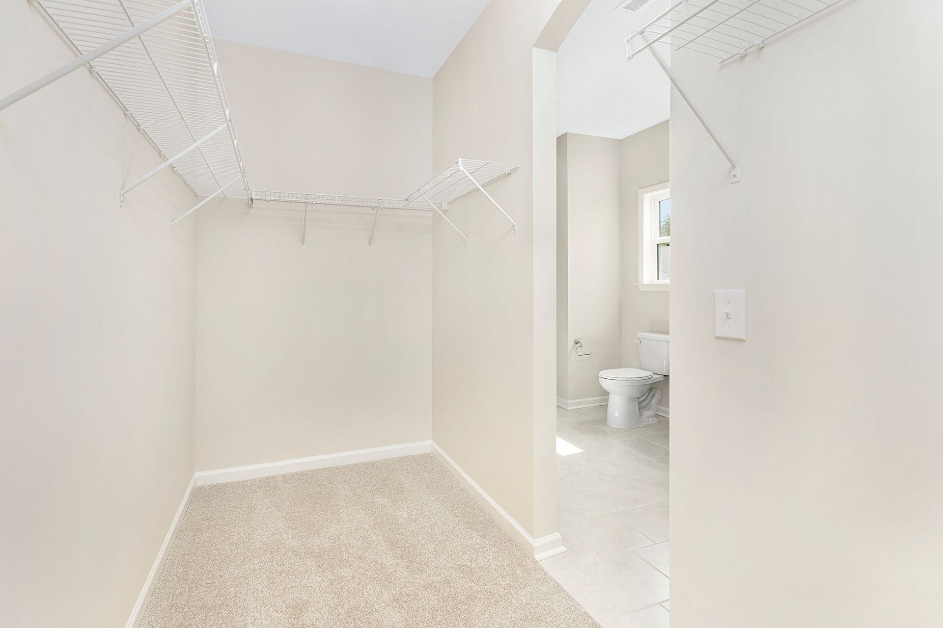 An empty walk in closet with a toilet and a window.