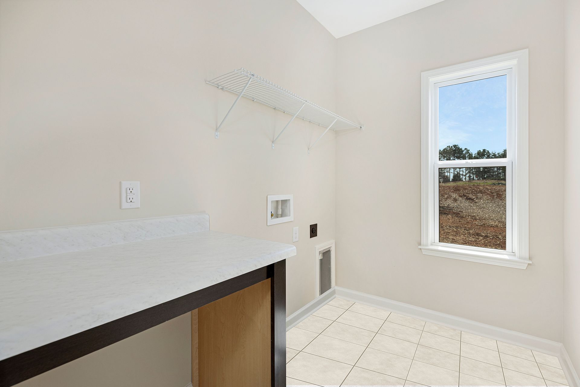 An empty laundry room with a window and a shelf.
