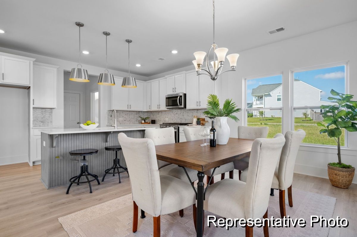 A dining room with a table and chairs and a kitchen in the background.