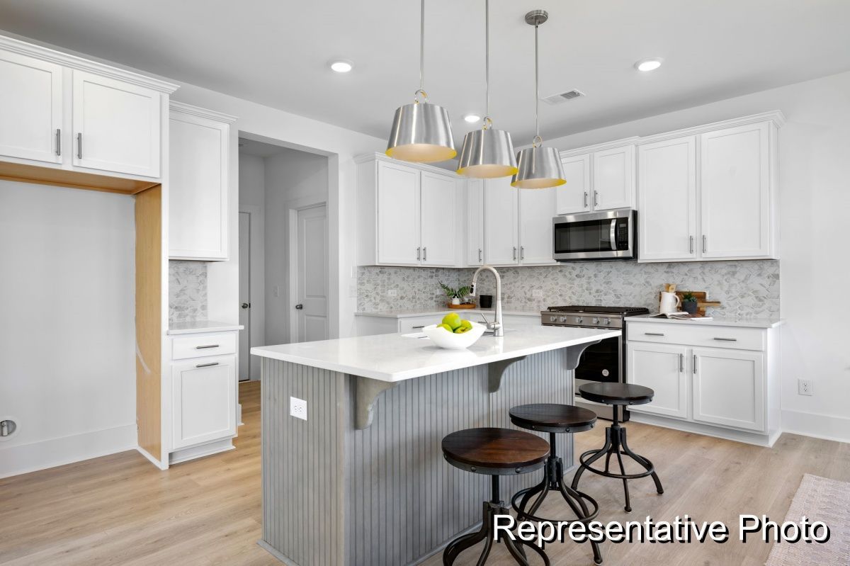 A kitchen with white cabinets , a large island , stools and a microwave.