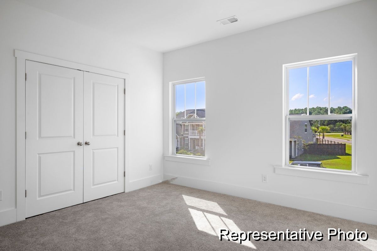 An empty bedroom with two windows and a carpeted floor.