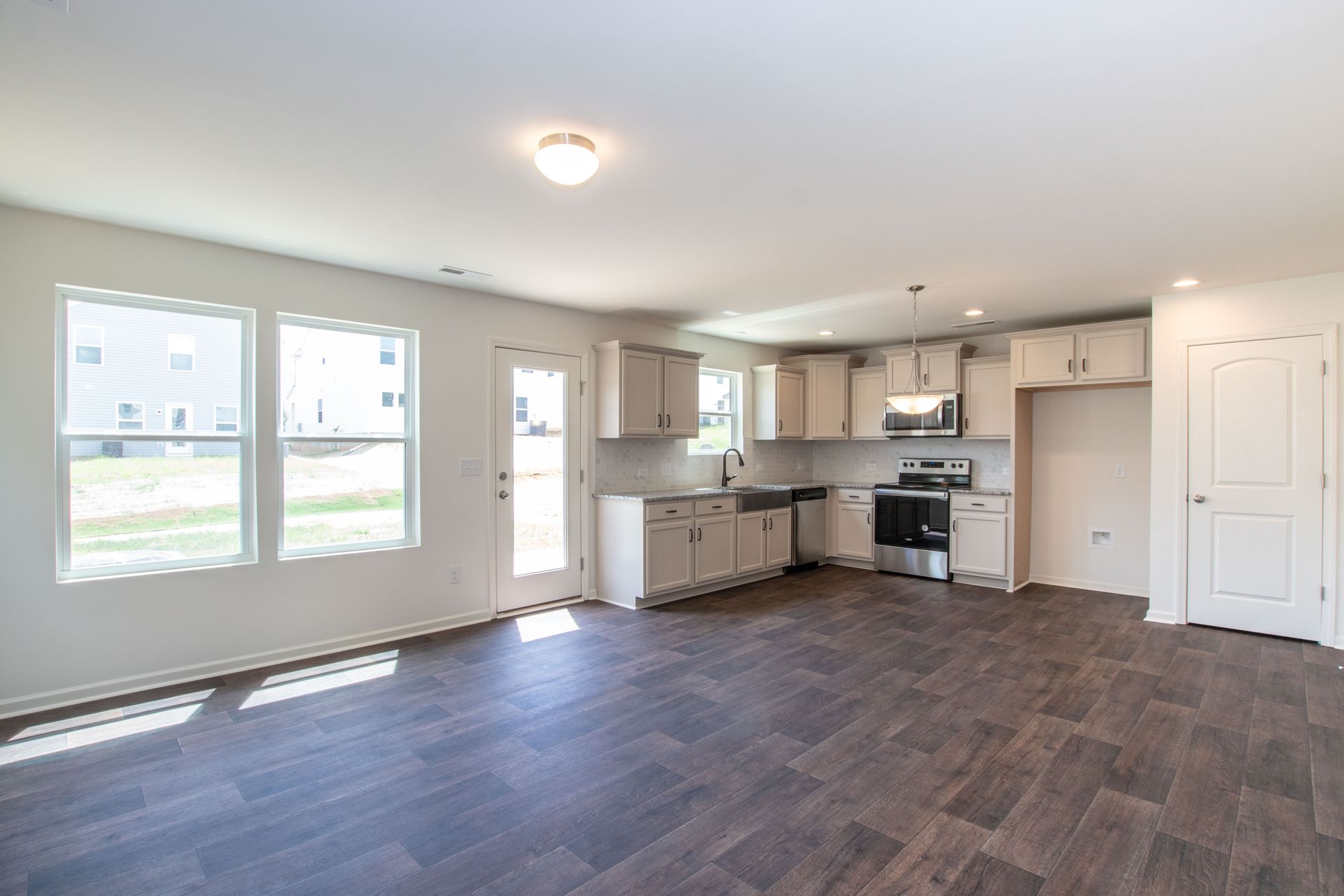 An empty living room with hardwood floors and a kitchen.