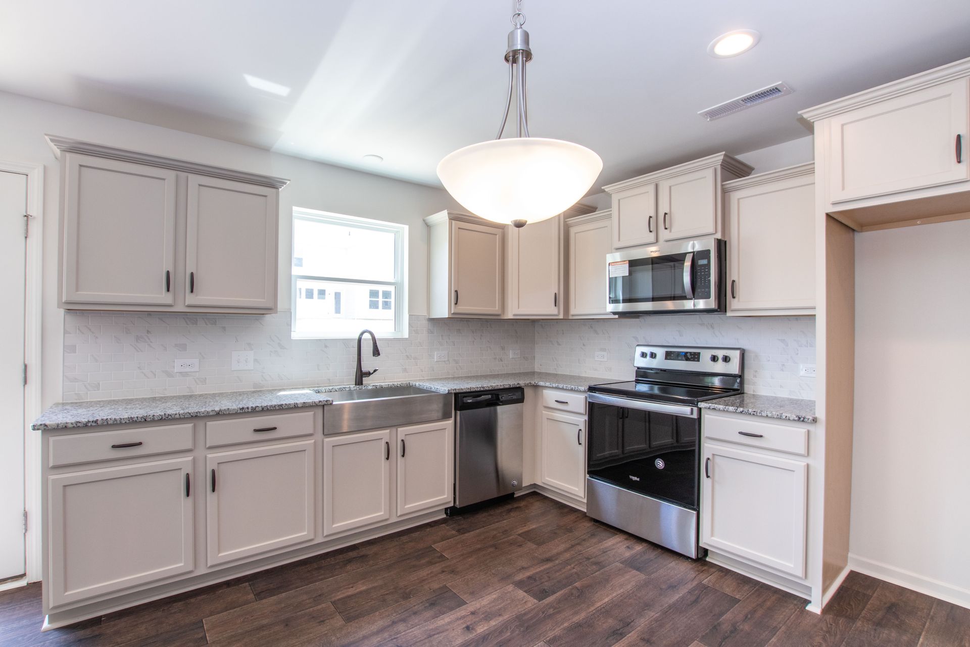 An empty kitchen with white cabinets and stainless steel appliances.
