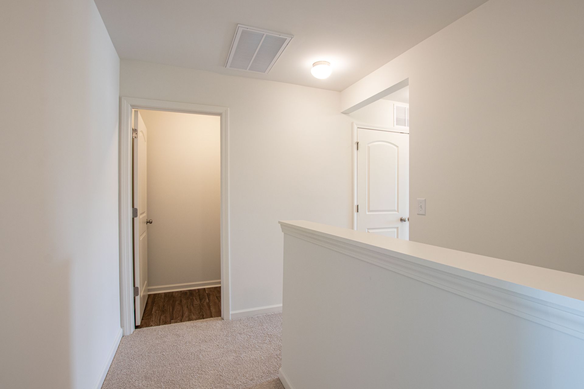 A hallway with a staircase leading to a closet in a house.