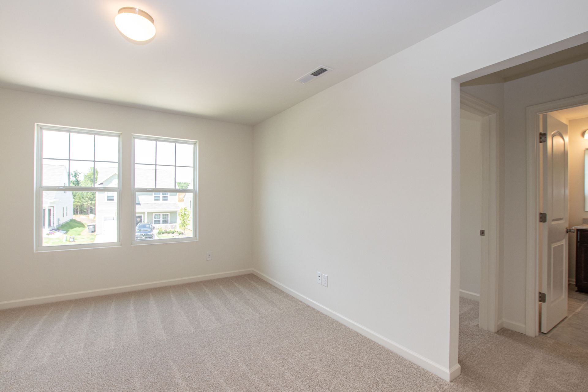 An empty bedroom with a carpeted floor and two windows.