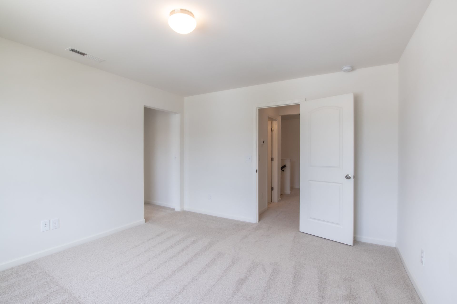 An empty bedroom with a carpeted floor and white walls