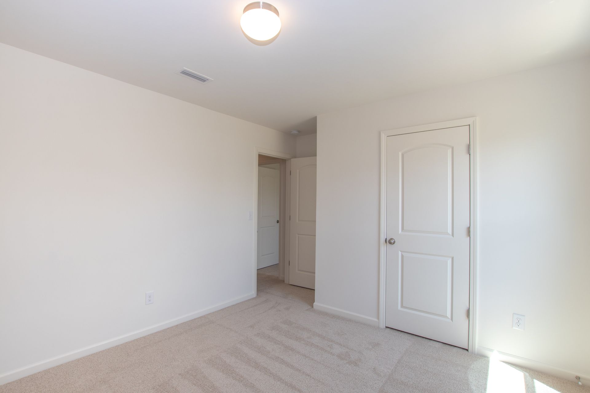 An empty bedroom with a door and a light on the ceiling.