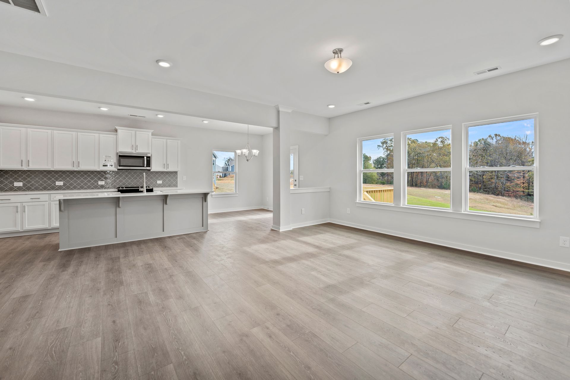 An empty living room with hardwood floors and a kitchen in the background.