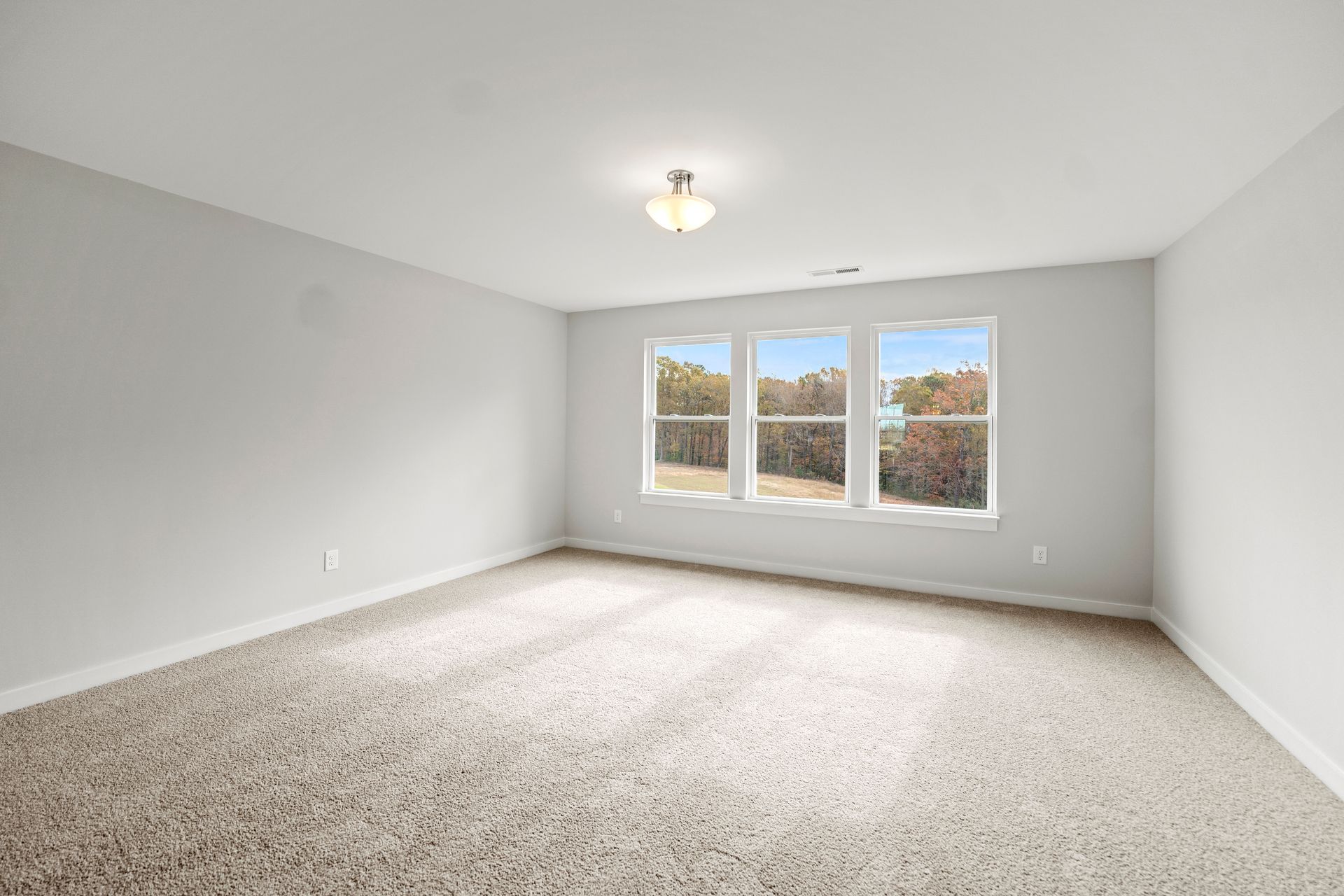An empty room with a carpeted floor and three windows.