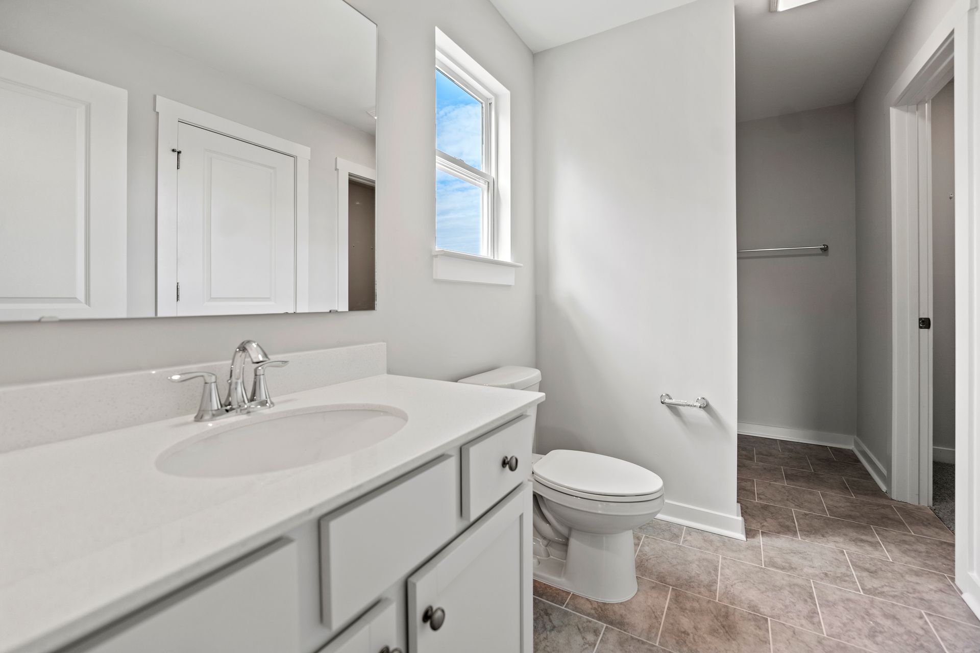 A bathroom with a sink , toilet , mirror and window.