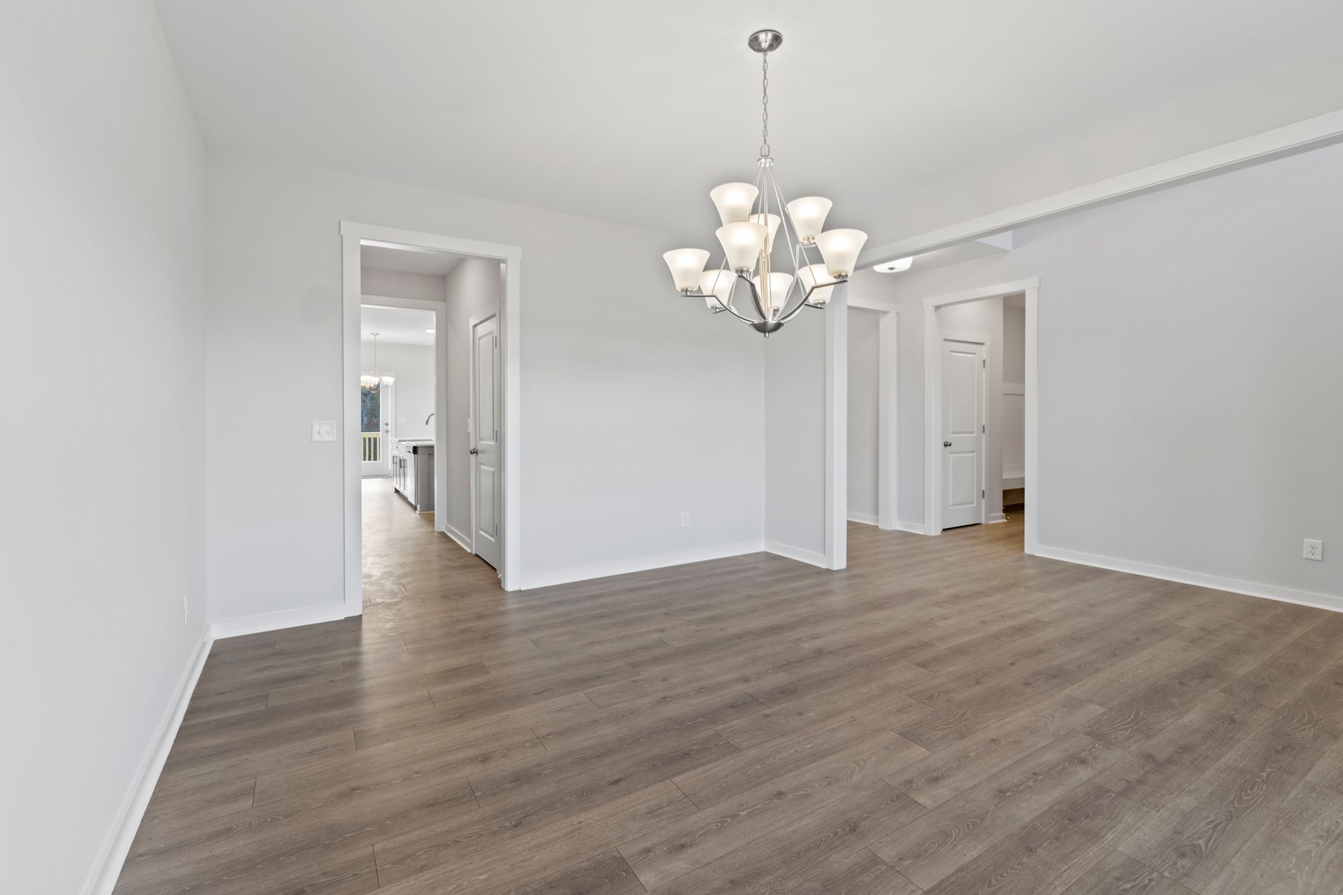 An empty dining room with hardwood floors and a chandelier.