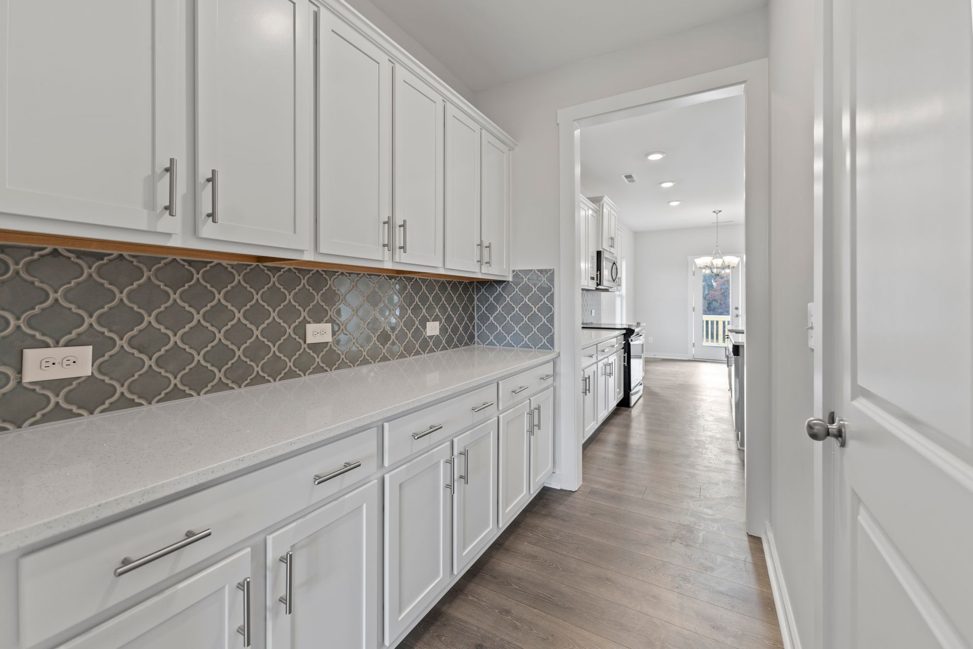 A kitchen with white cabinets and gray tiles on the wall.