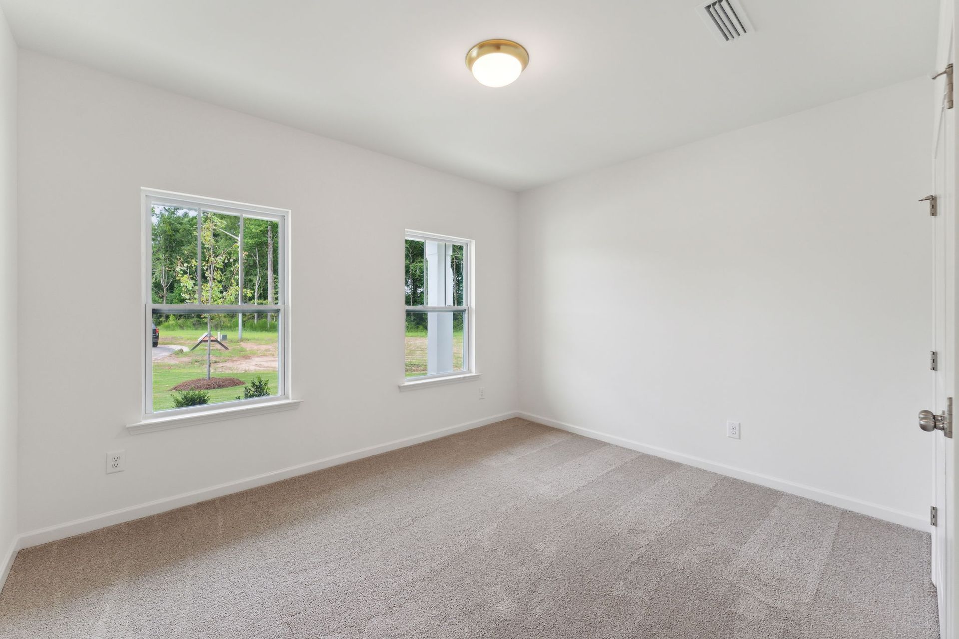 An empty bedroom with a carpeted floor and two windows.
