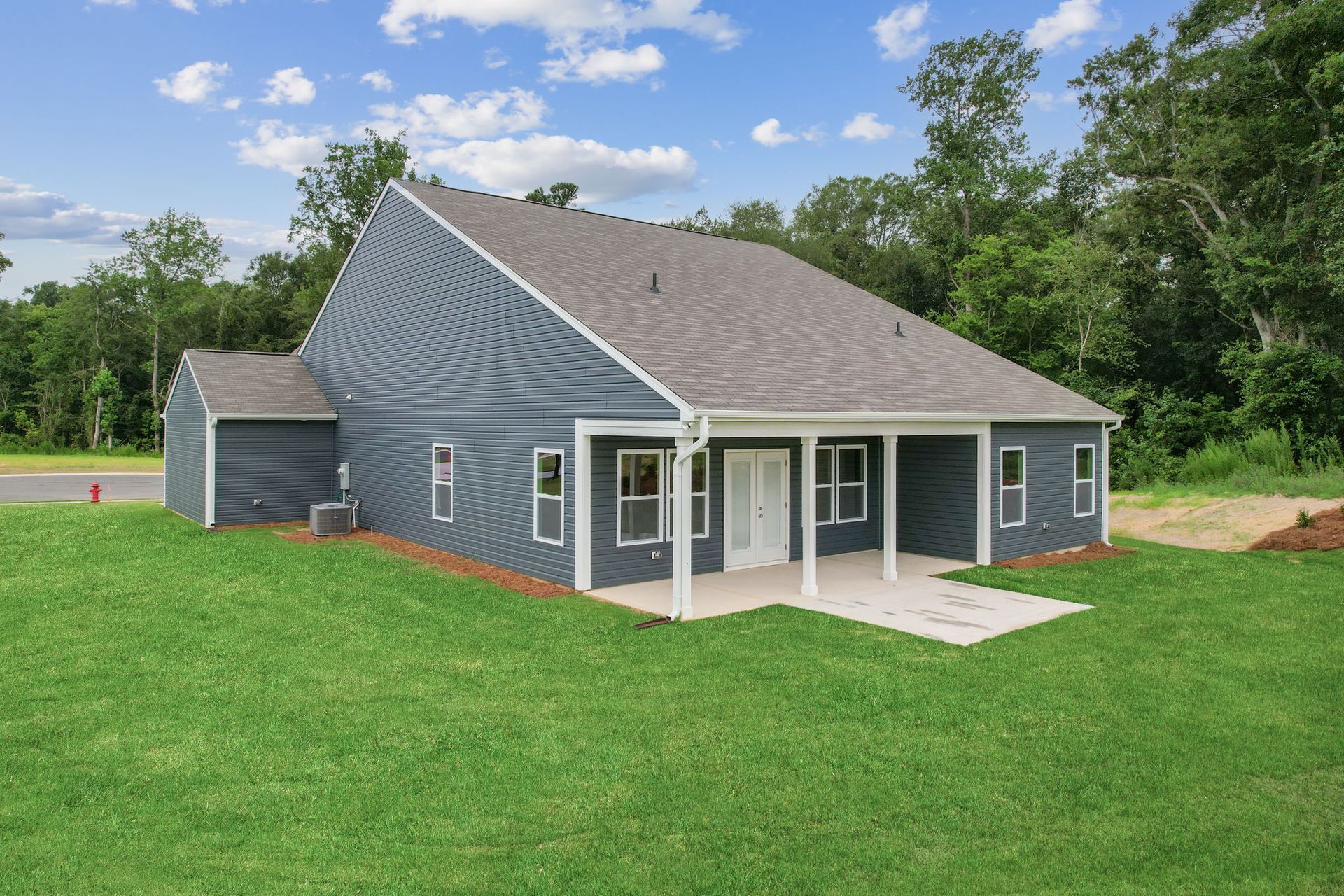 A blue house with a porch is sitting on top of a lush green field.