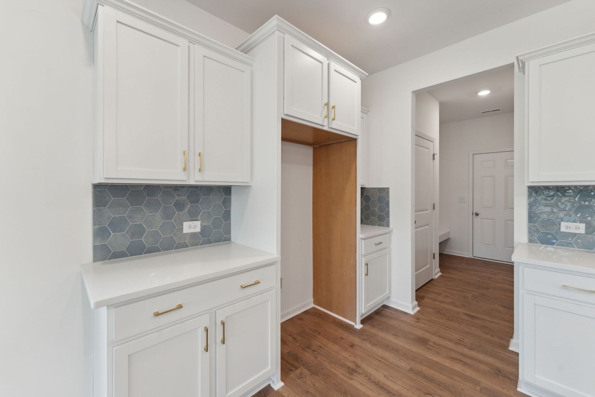 A kitchen with white cabinets , hardwood floors , and a refrigerator.
