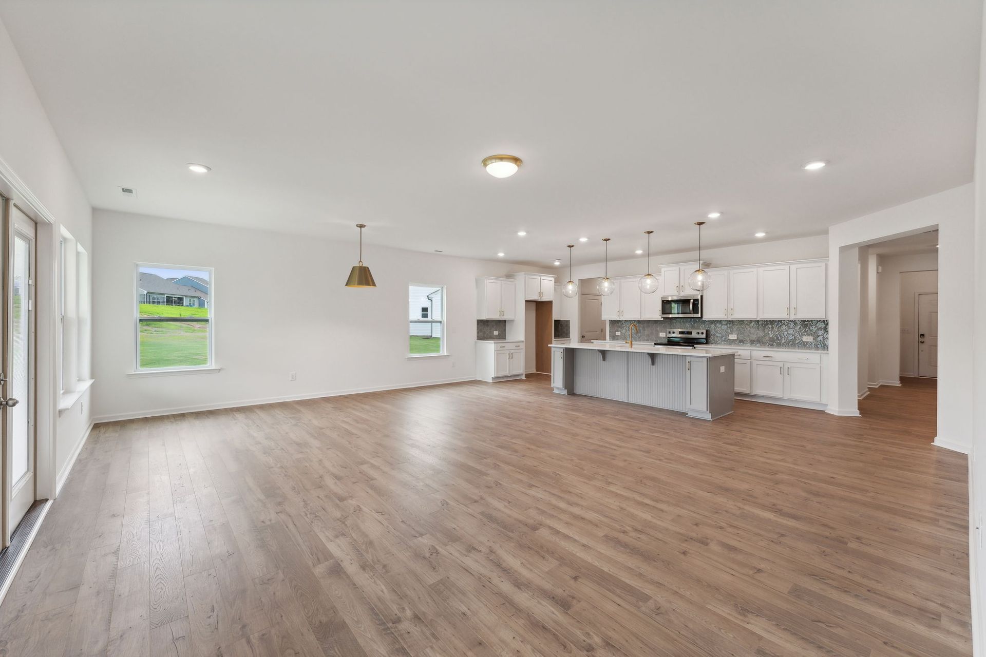A large empty room with hardwood floors and a kitchen.