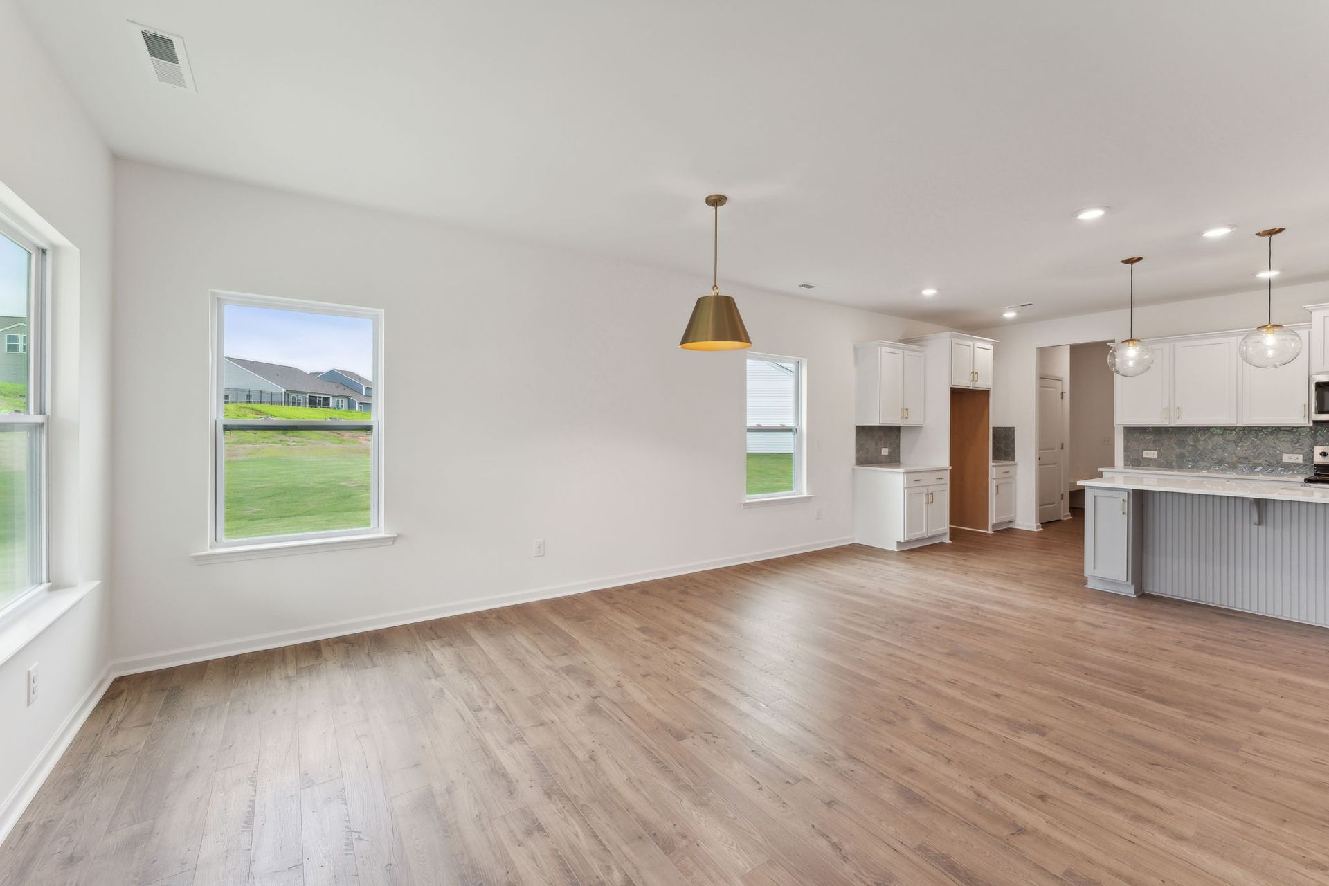 An empty living room with hardwood floors and a kitchen in the background.