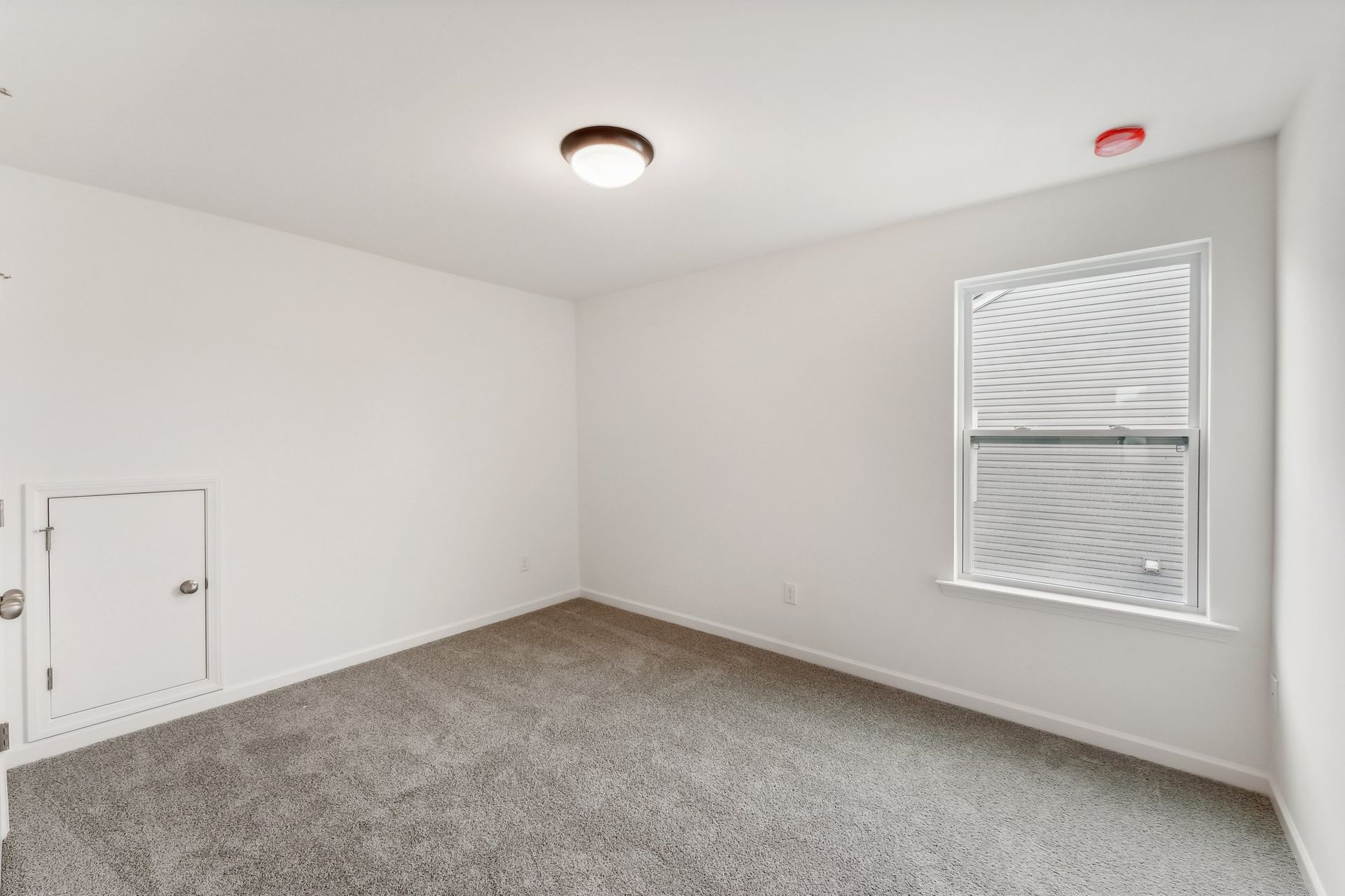 An empty bedroom with a window and a carpeted floor.