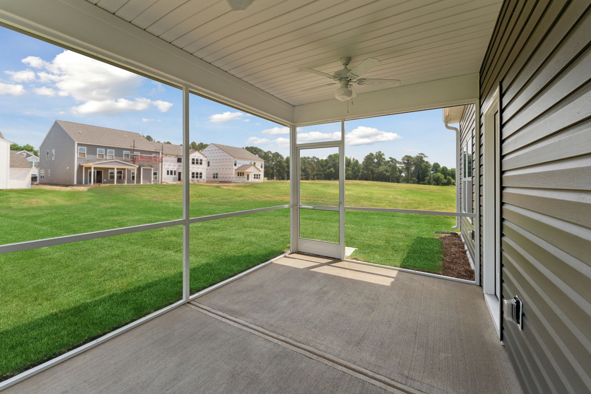 A screened in porch with a ceiling fan and a view of a lush green field.